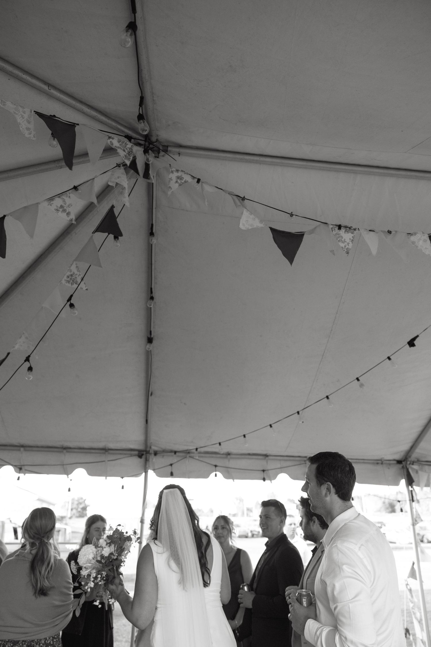 A black and white photo of a wedding celebration under a tent with hanging decorations.