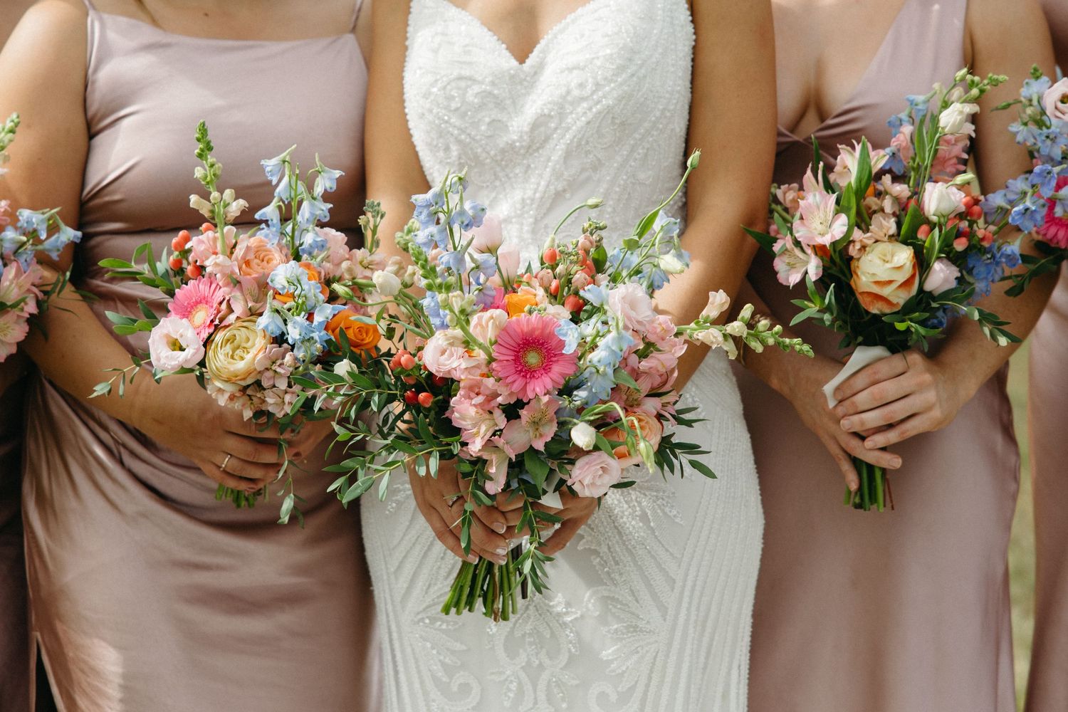 Bridesmaids in blush dresses holding colorful floral bouquets.