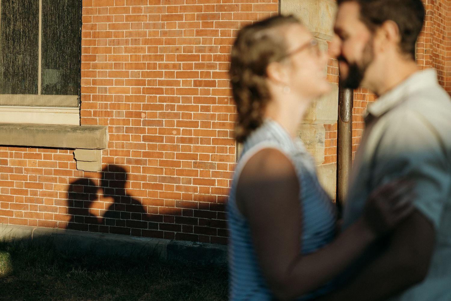 Silhouettes embrace against a brick wall in warm evening light.