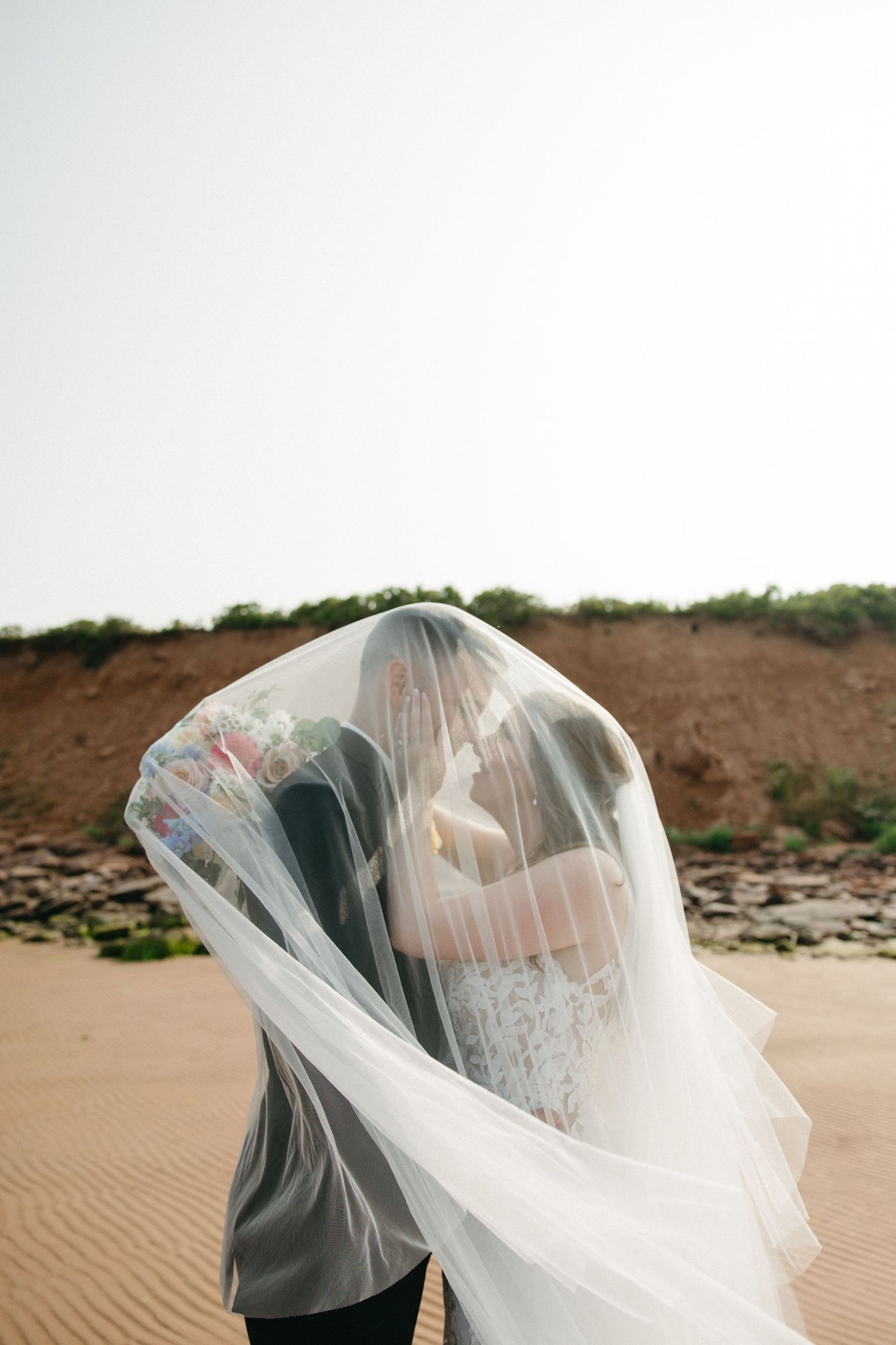 Artistic wedding veil shot with natural beach scenery in background.