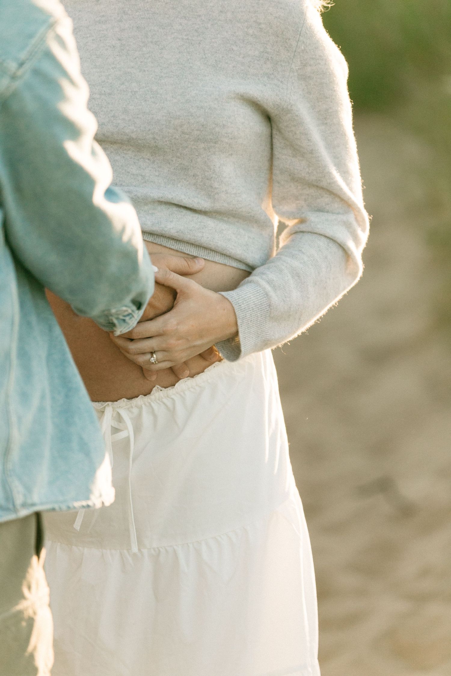 Close-up of hands tenderly cradling a pregnant belly in soft lighting.