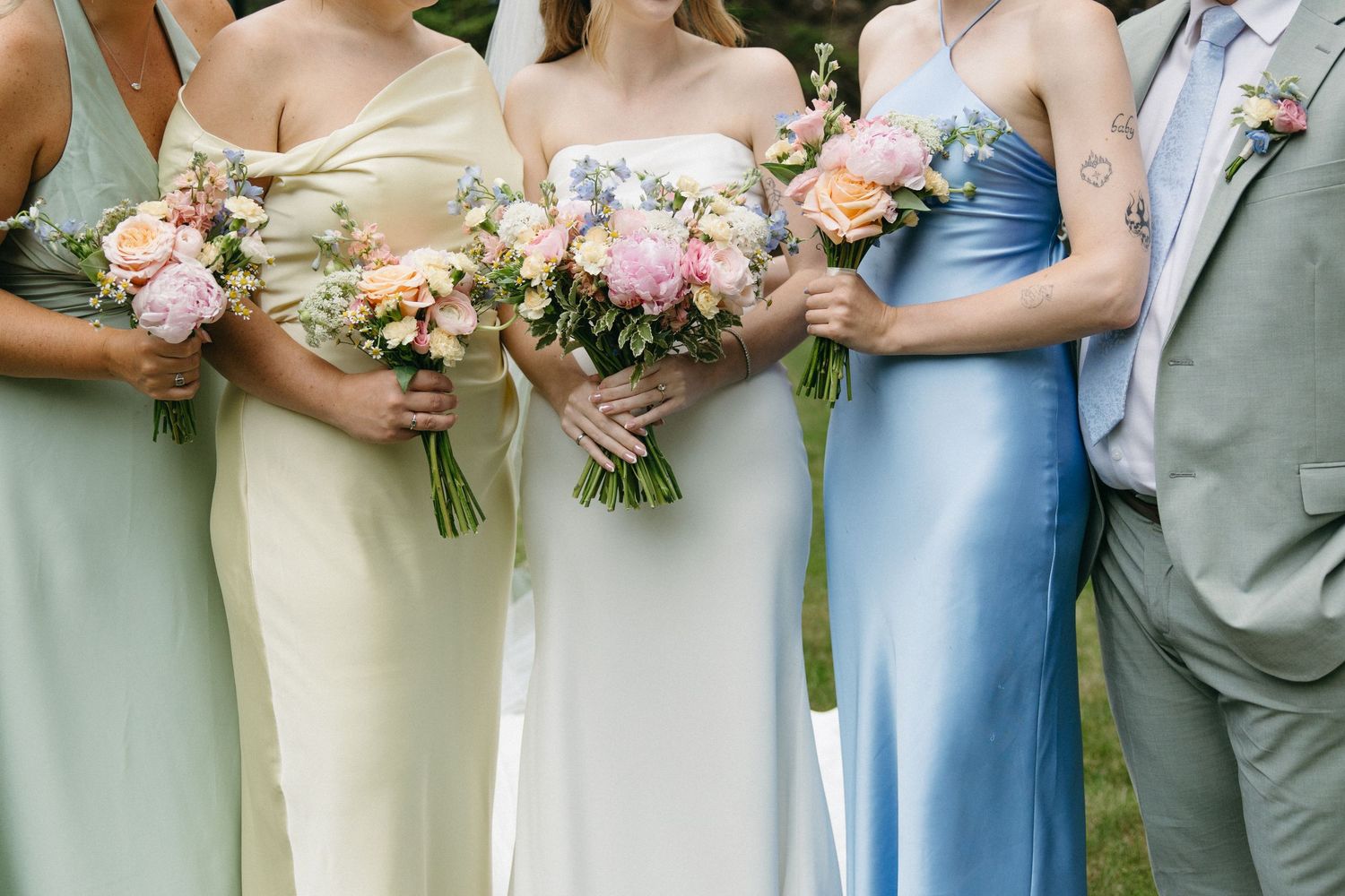 A bride and bridesmaids in pastel satin dresses holding colorful spring wedding bouquets.