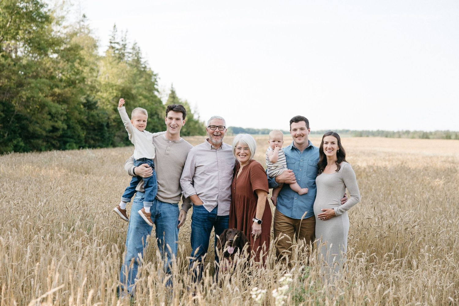 Large multigenerational family of seven posing together in a golden wheat field outdoors.