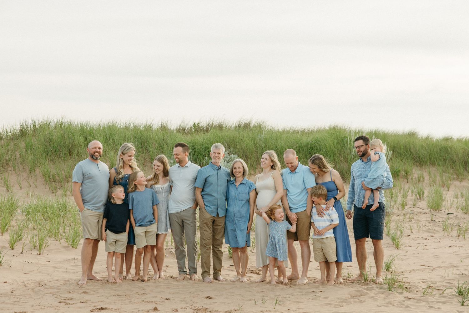 A large extended family in coordinating blue outfits poses together on a sandy beach.