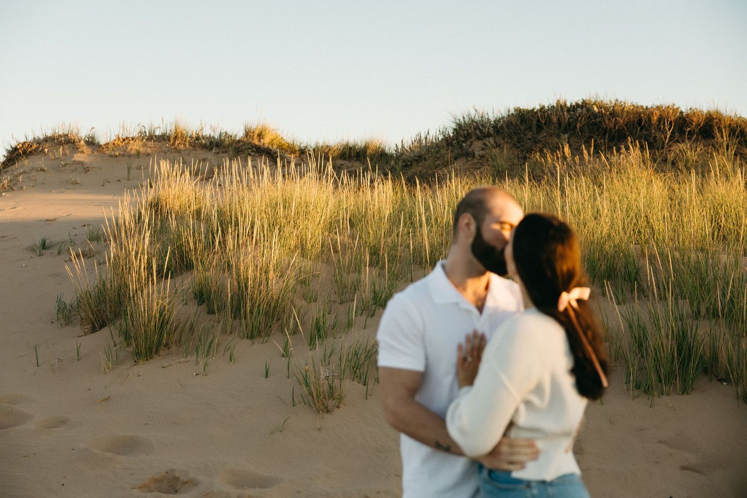 Romantic beach photoshoot among coastal grass during golden hour.