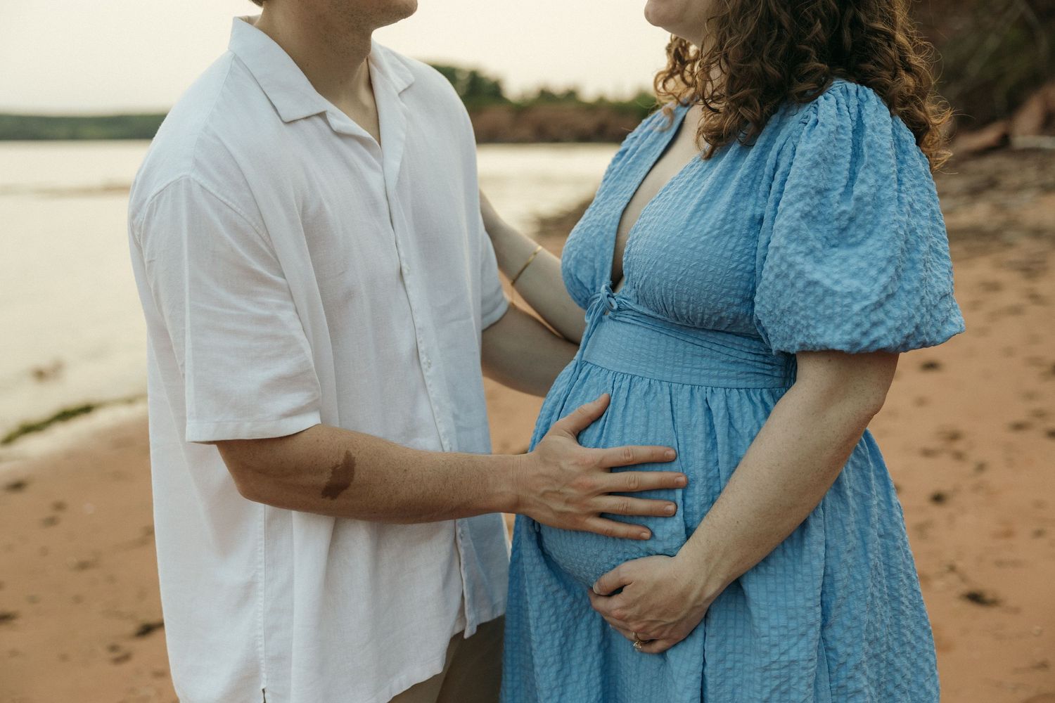 A couple in white and blue attire embrace on a sunny beach.