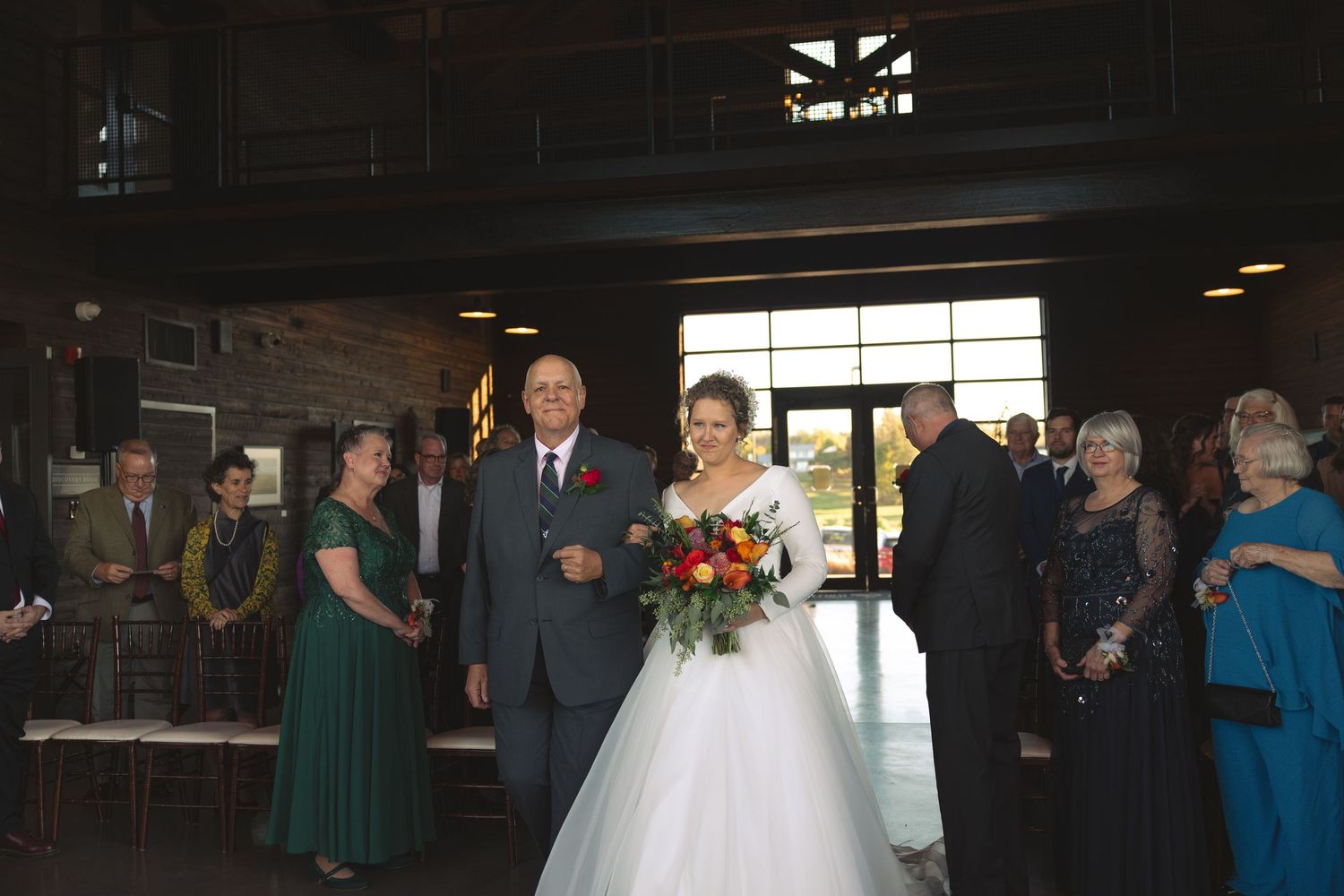 Wedding reception guests mingle in dark indoor venue with ambient lighting.