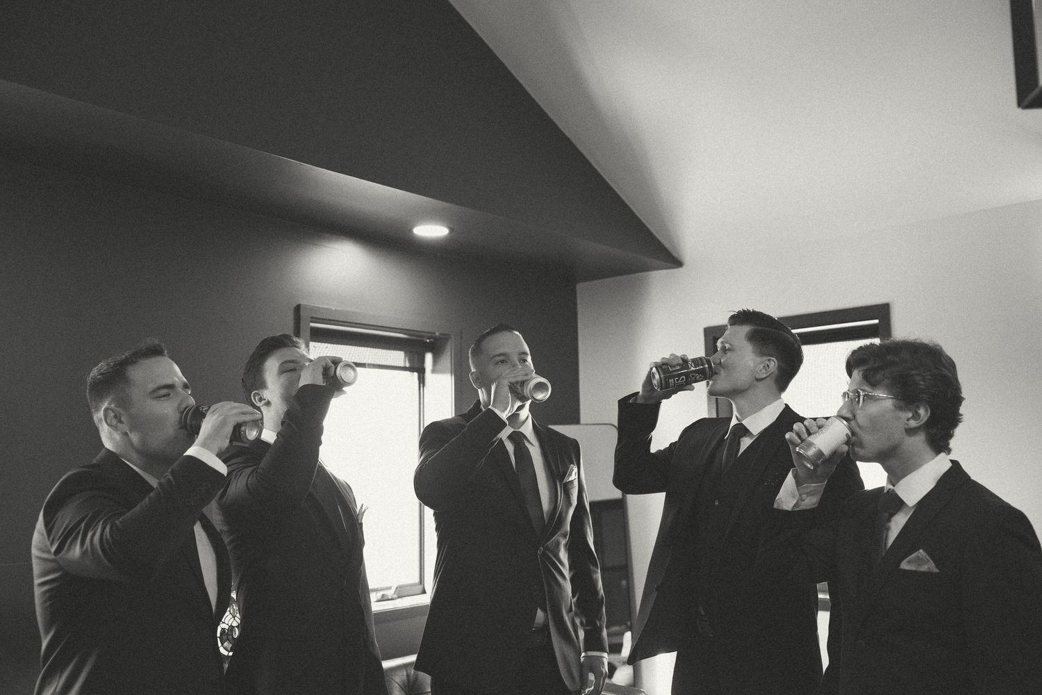 Groomsmen interact in a naturally lit room during wedding preparations.