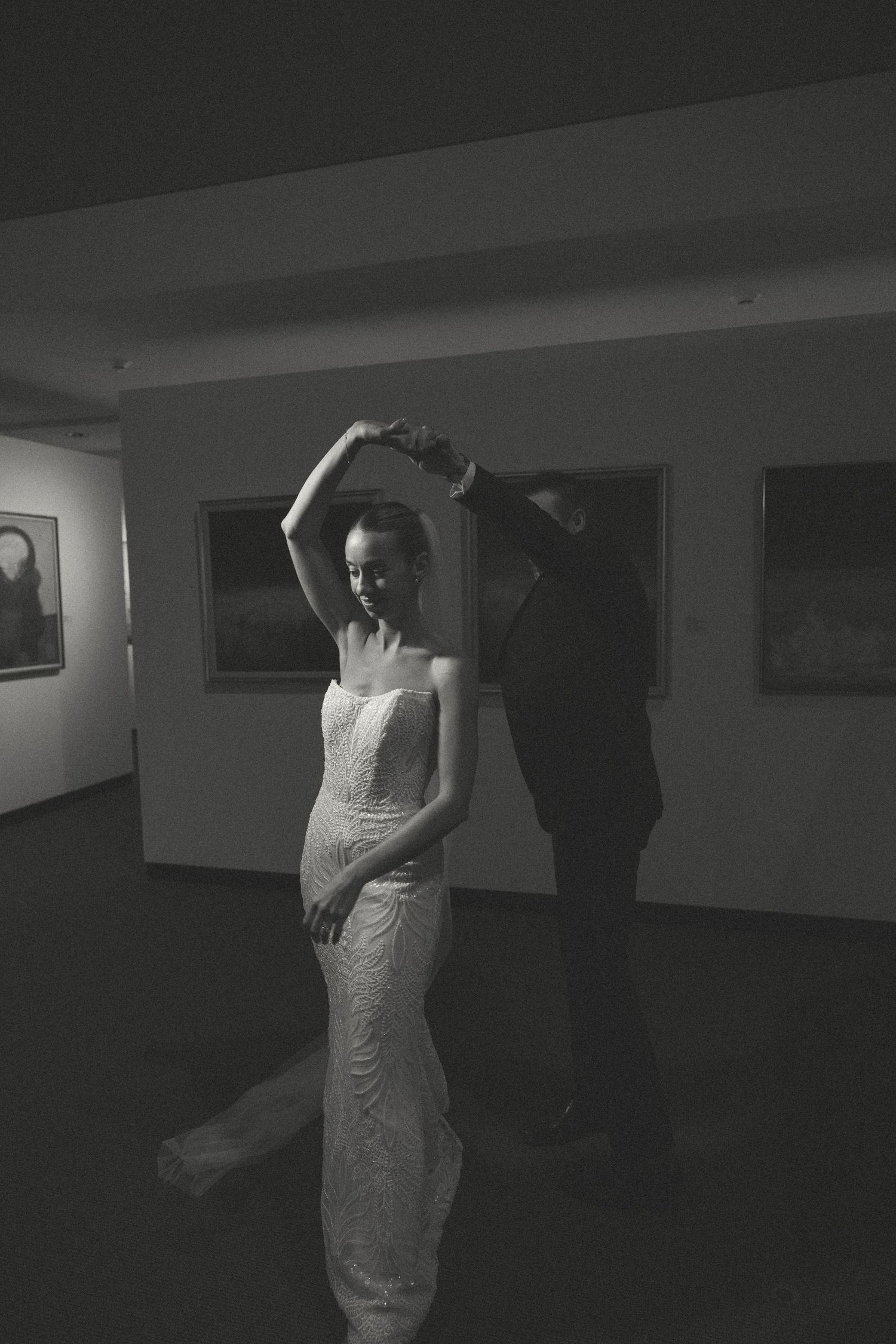 A couple sharing an intimate dance in a dimly lit room with white walls.