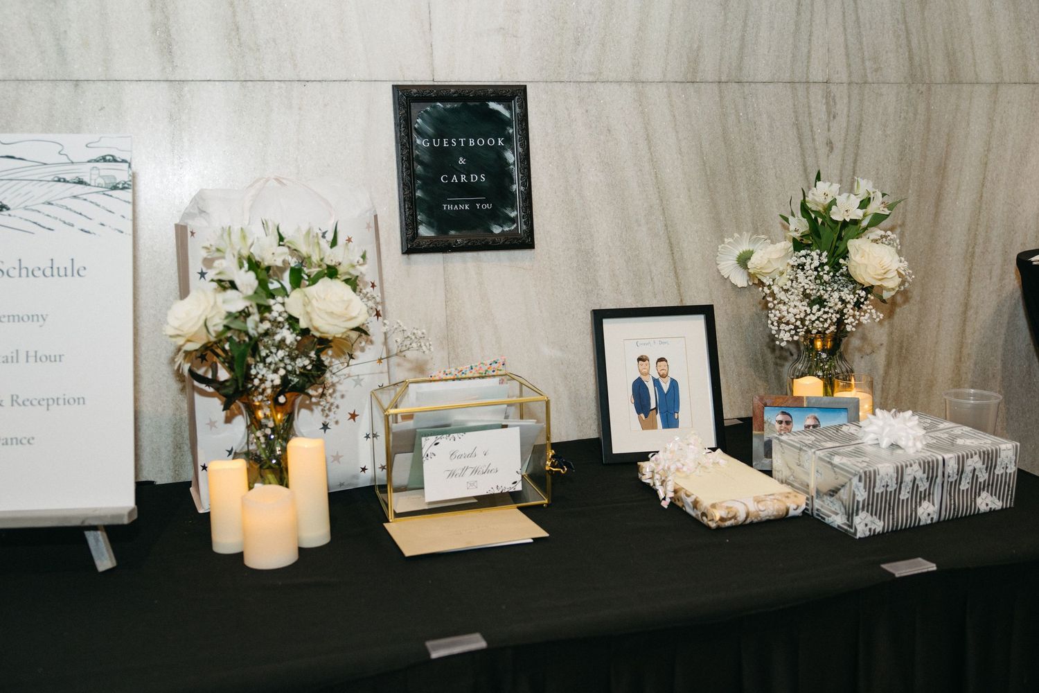 Wedding reception welcome table with white floral arrangements and decorative items on black tablecloth.
