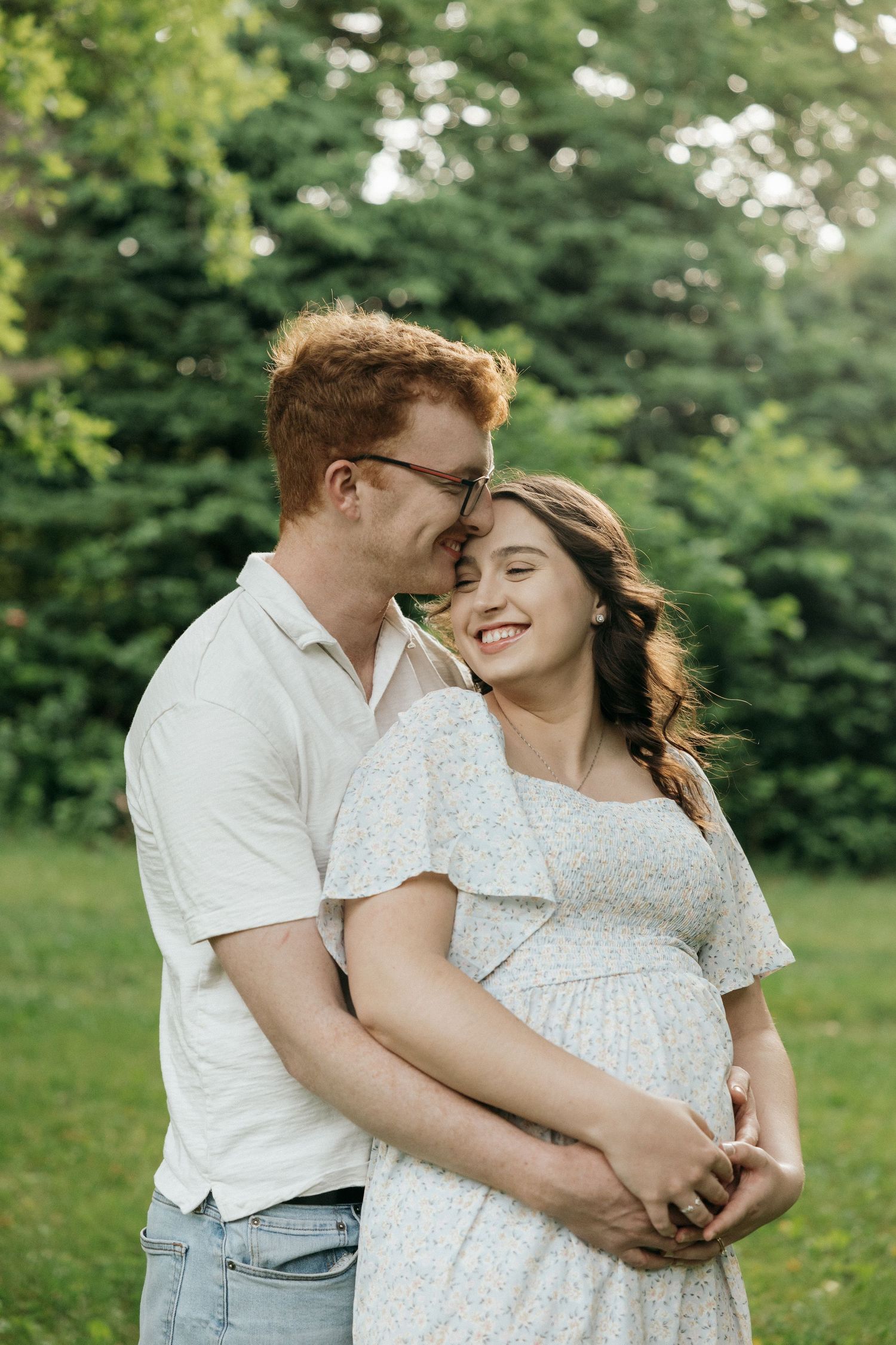 A tender moment between a couple in white clothing against a lush green summer backdrop.