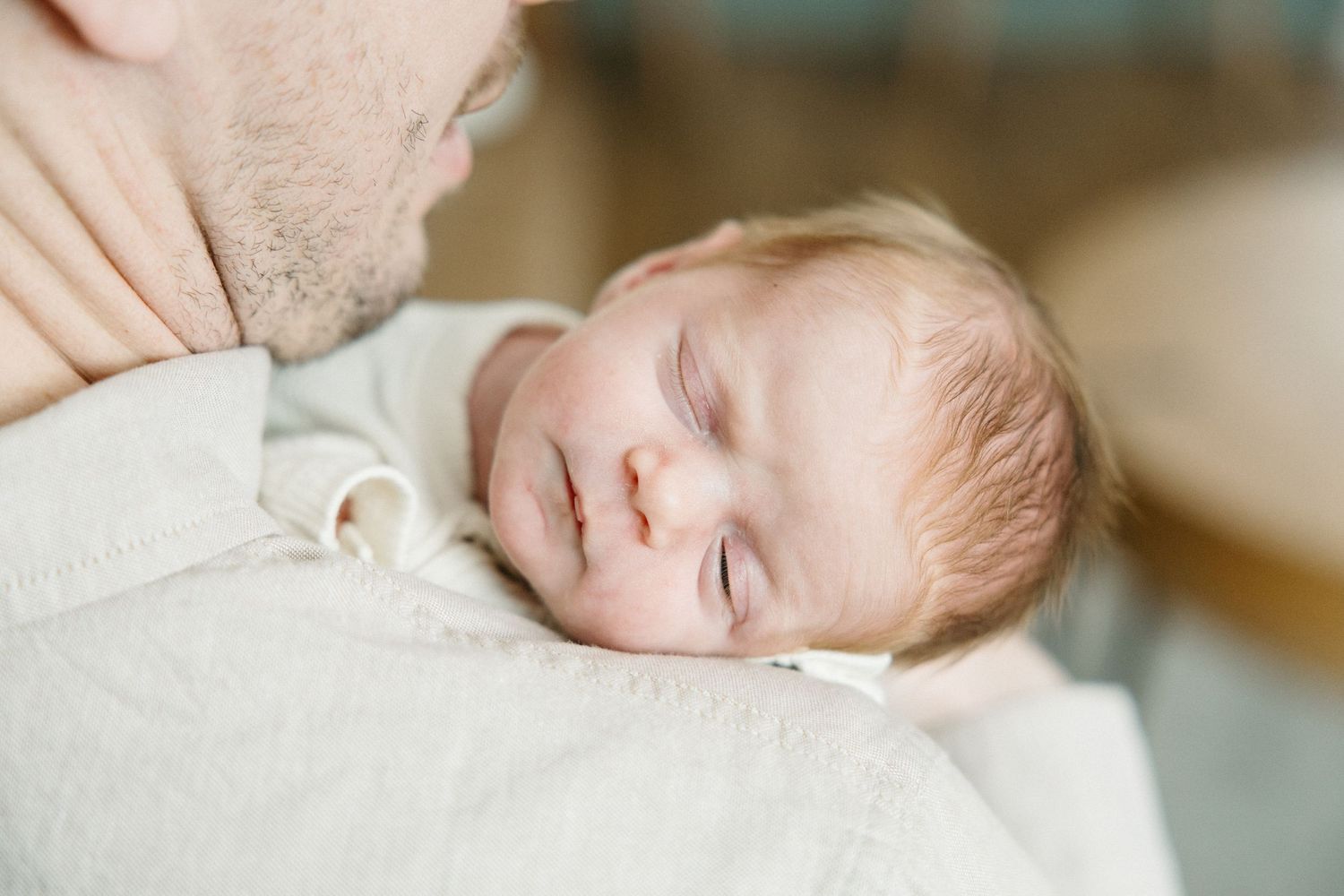 Close up of sleeping infant with soft natural light on white bedding.