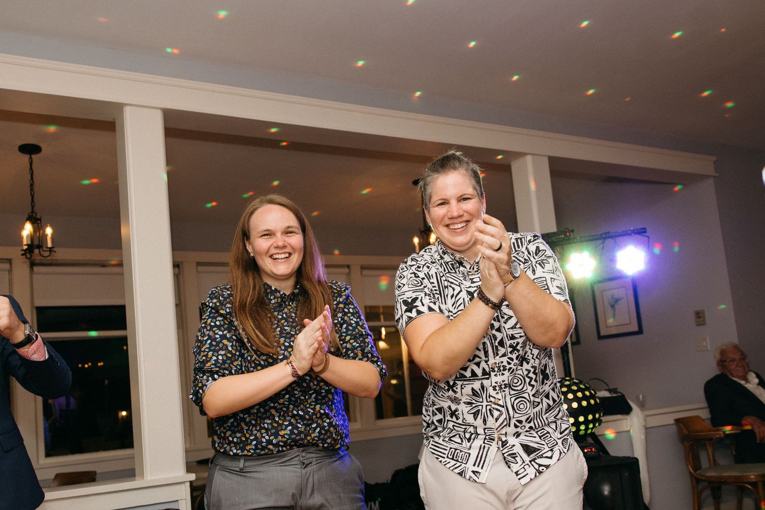 Two women laughing and clapping together on wedding reception dance floor.