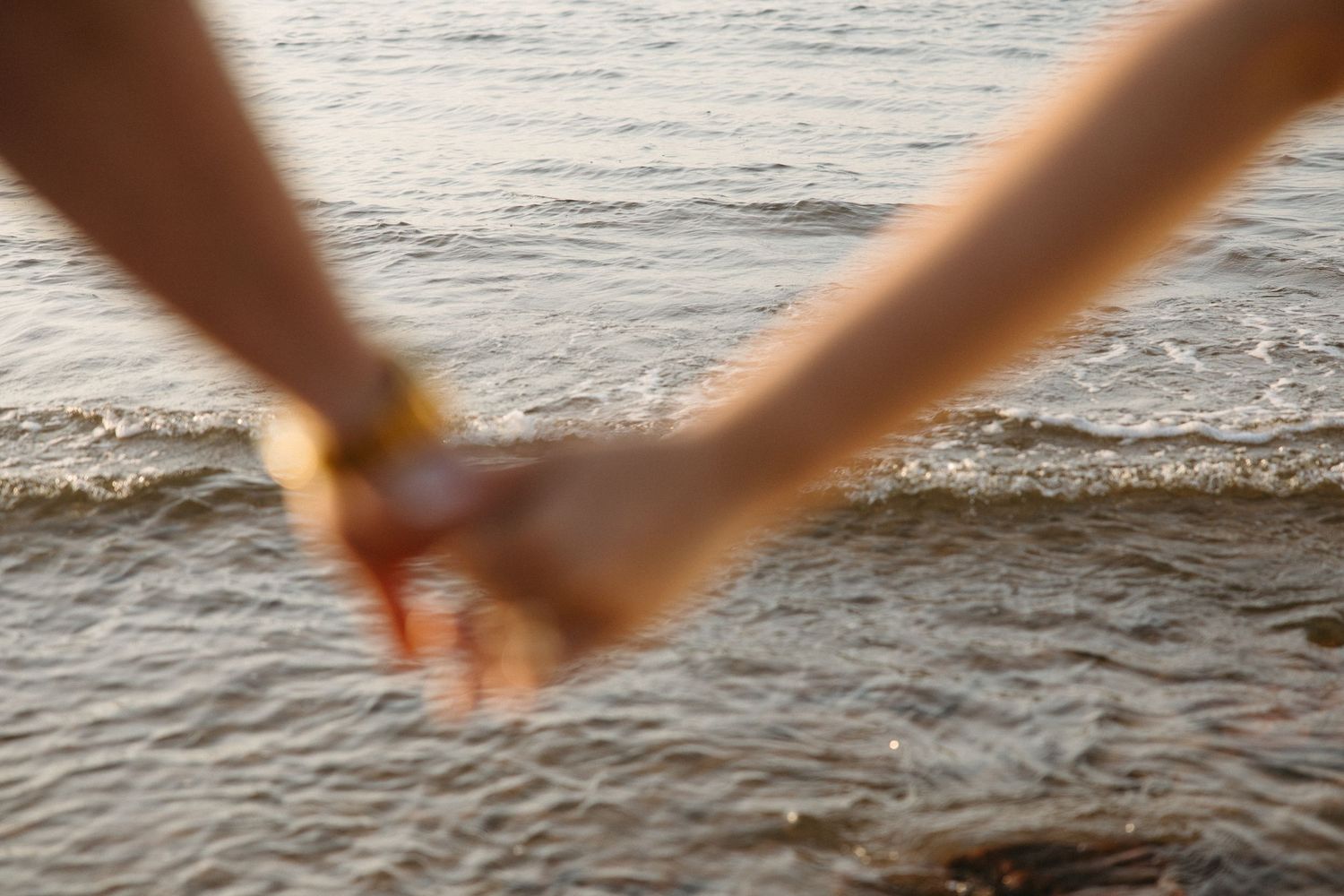 Close-up of couple holding hands at waters edge with gentle ocean waves in the background.