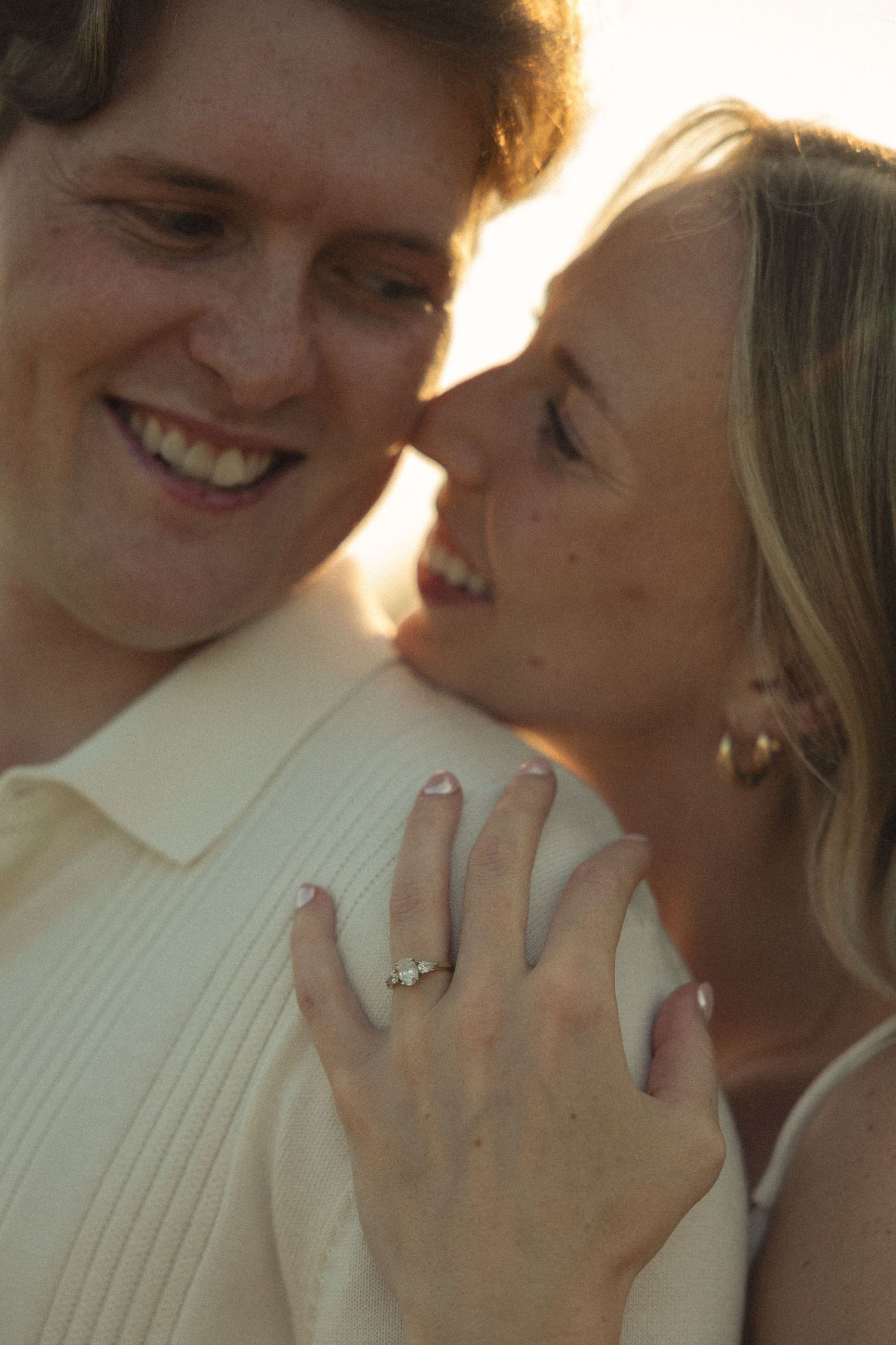 Close-up of happy couple with woman showing diamond engagement ring on her hand at sunset.