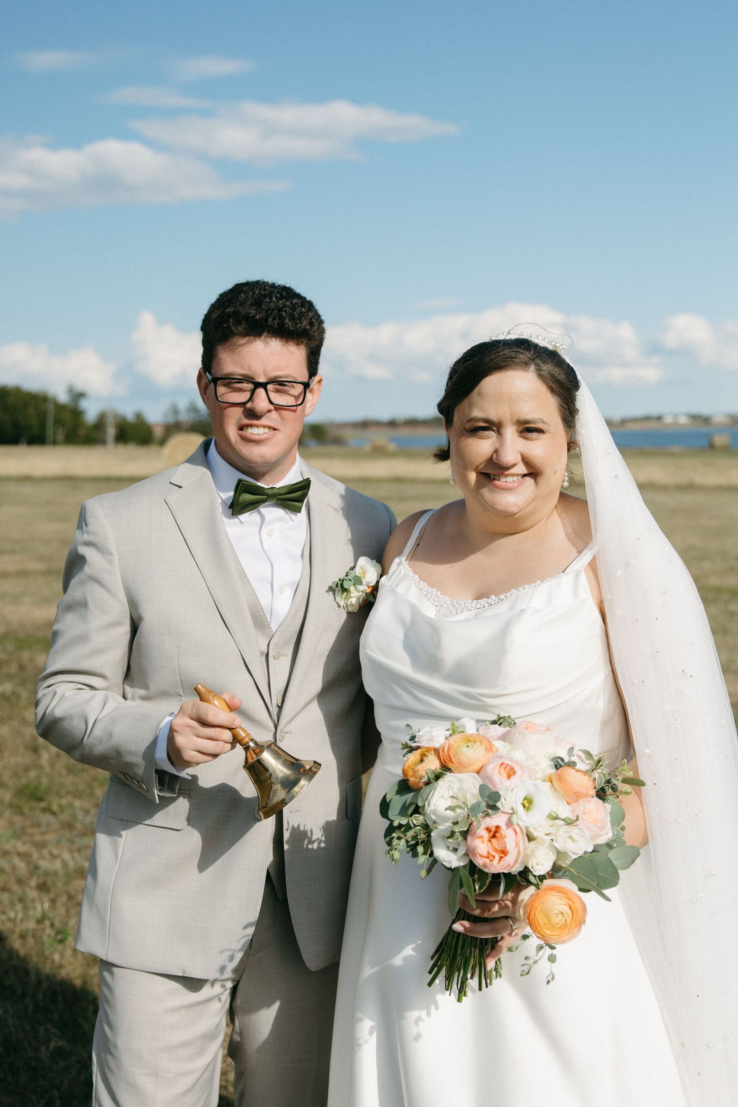 Smiling bride and groom posing outdoors on their wedding day, bride holding a peach and white bouquet.