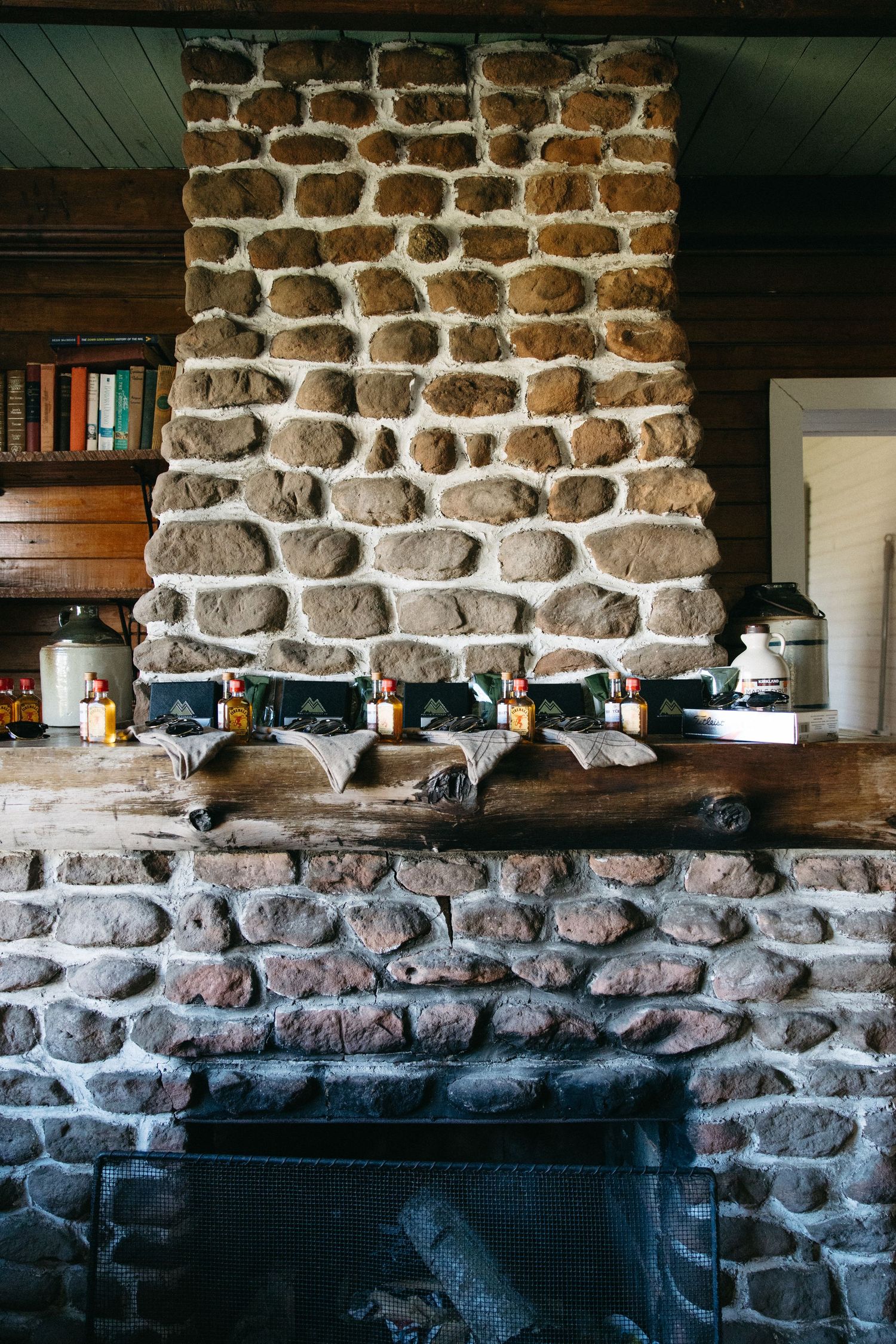 Rustic stone fireplace with wooden mantel decorated with small bottles in a cozy cabin interior.