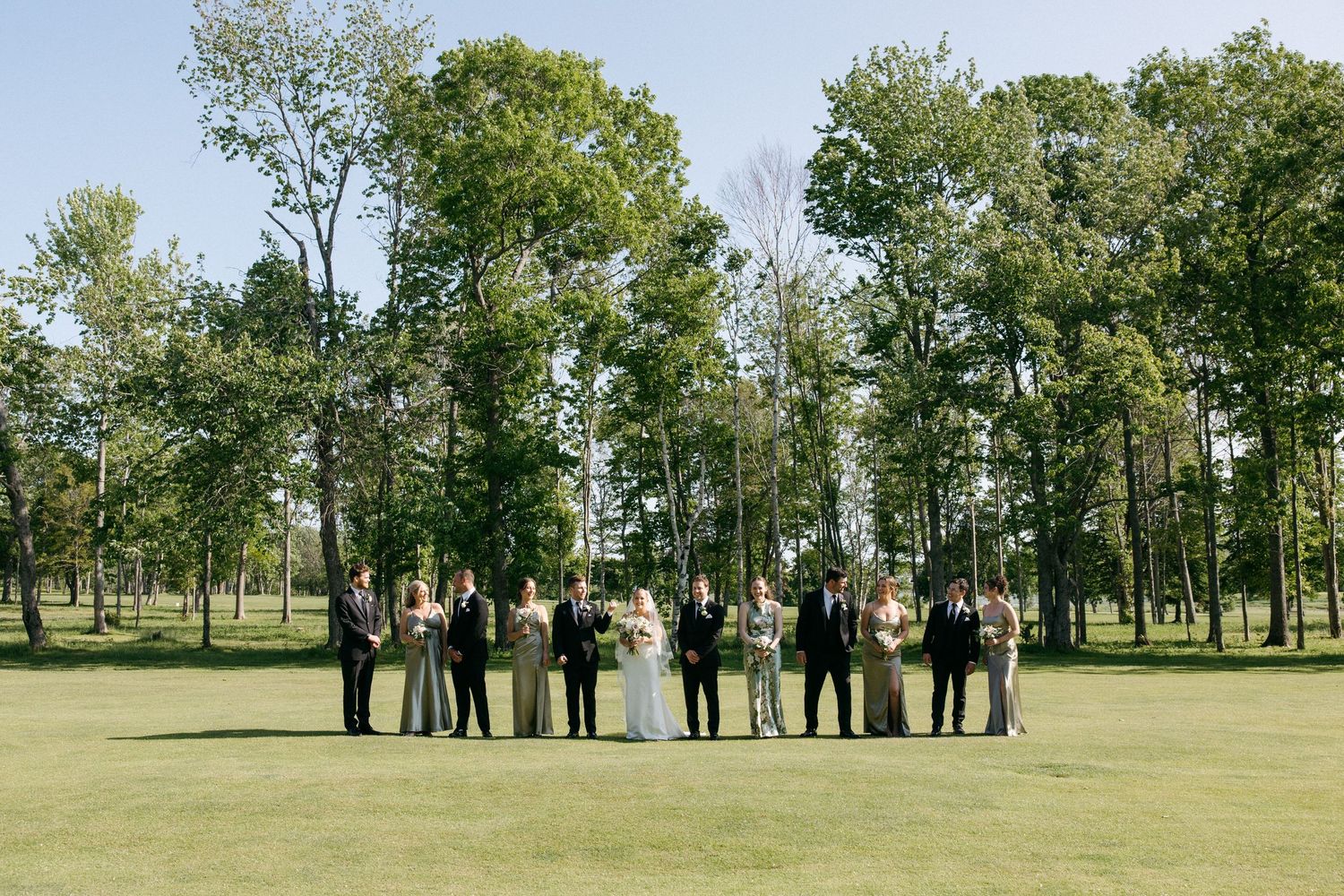 Wedding party lined up for photos outdoors with trees in the background.