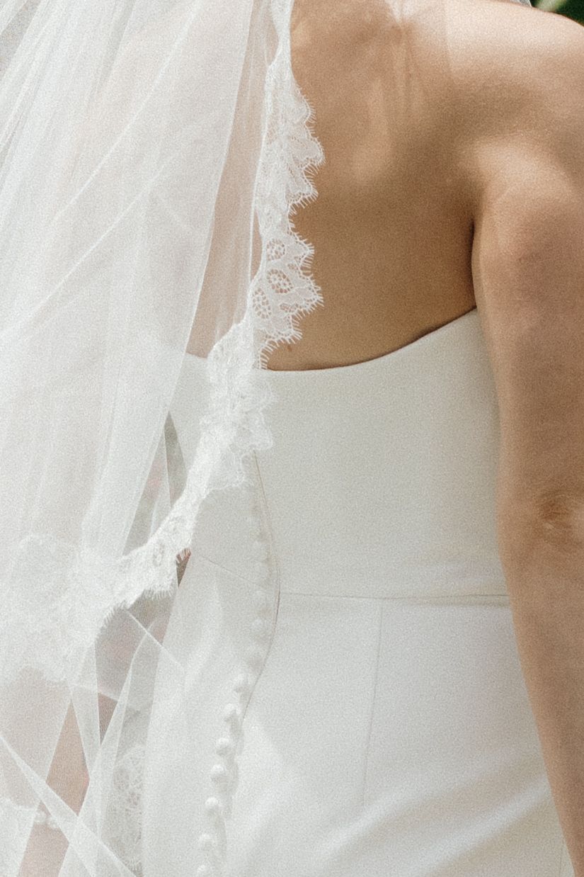 Close-up detail of delicate lace trim on a white wedding dress and veil.