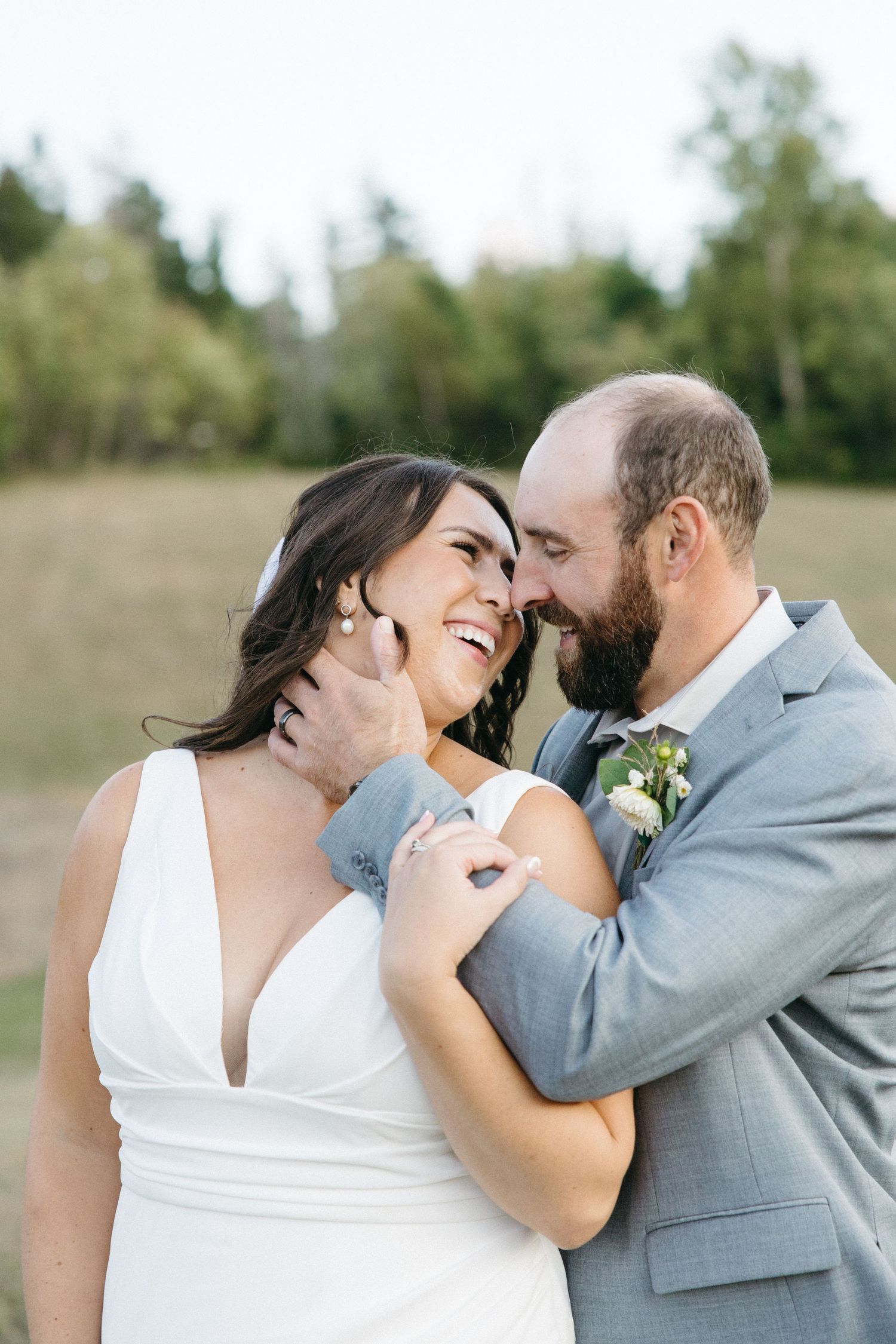 A couple laughs together during their outdoor wedding photoshoot on a sunny day.