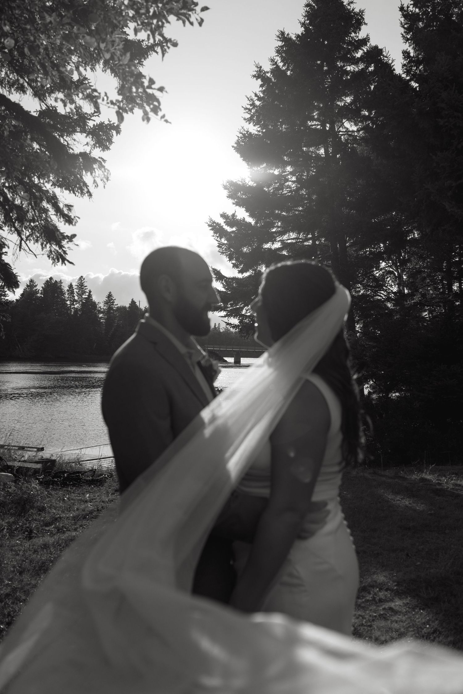 Black and white silhouette of couple against waterfront sunset.
