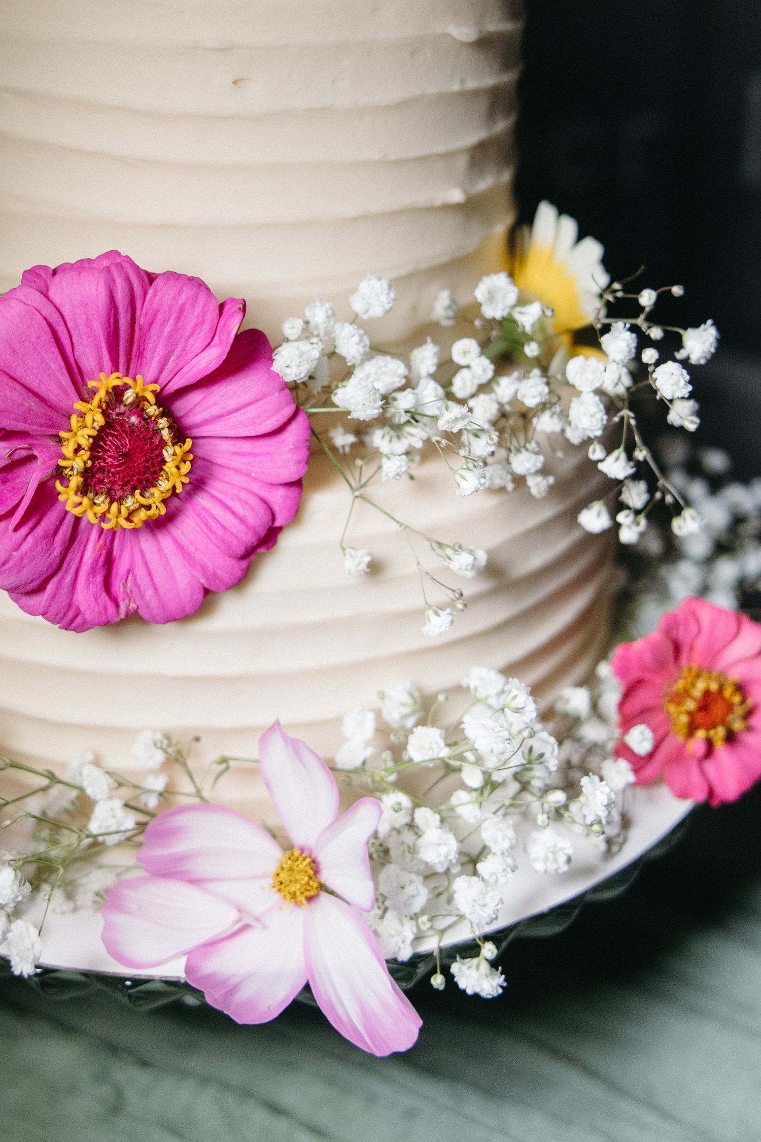 Wedding cake decorated with pink zinnias and delicate baby's breath flowers.