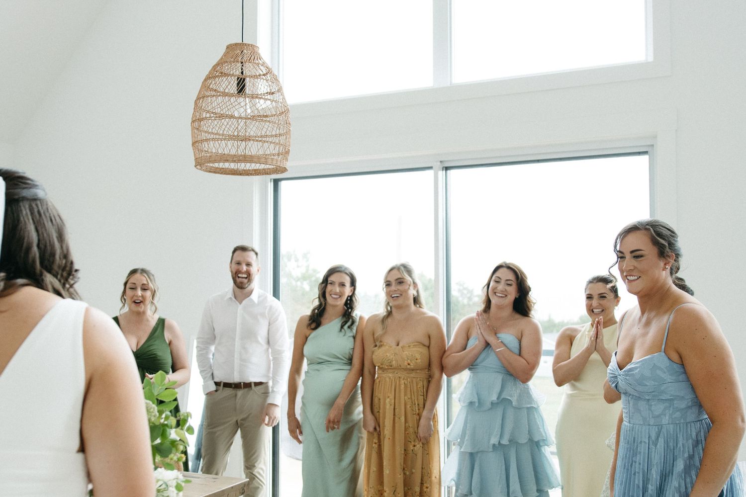 Wedding party members gather in a modern white room wearing pastel and neutral colored dresses.