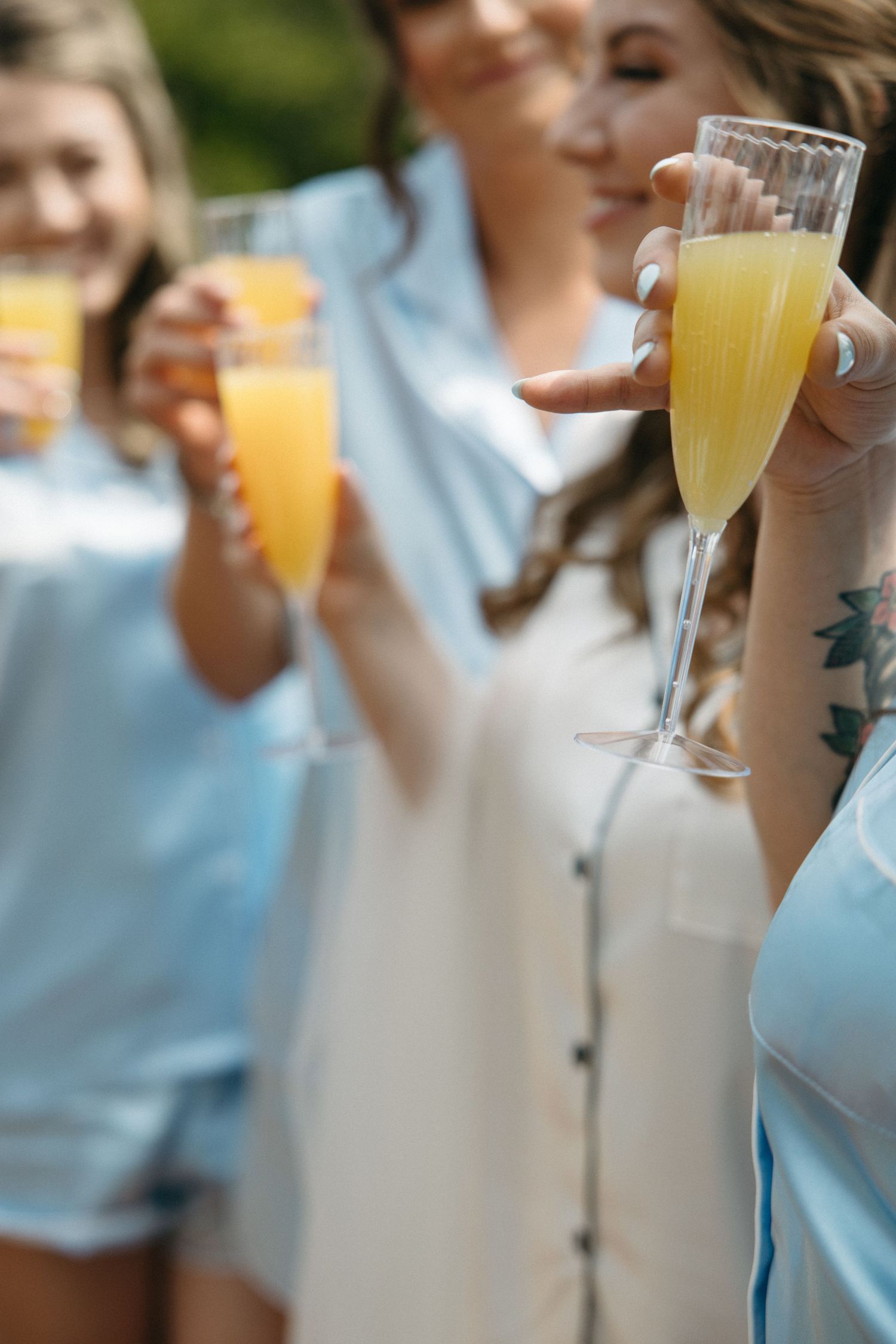 Hands holding mimosa glasses in a celebratory toast outdoors.