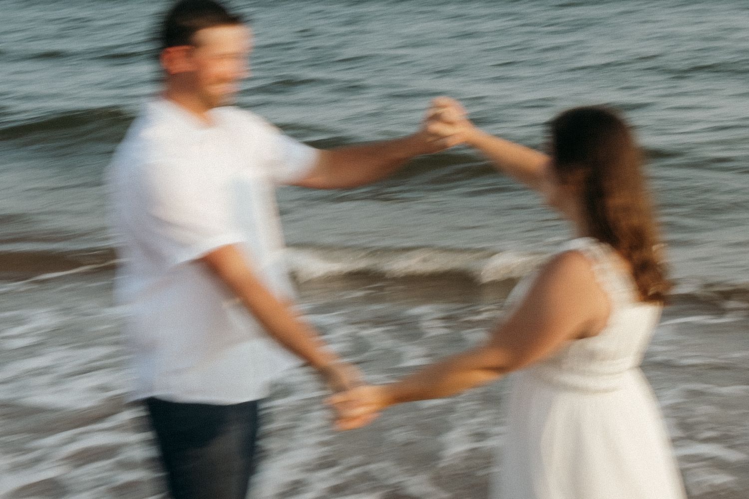 Couple dancing and spinning in the ocean waves at the beach.