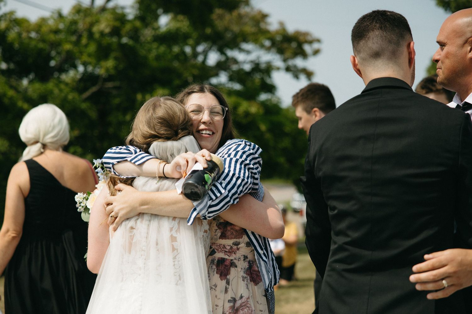 Wedding party members celebrate with hugs during outdoor reception.