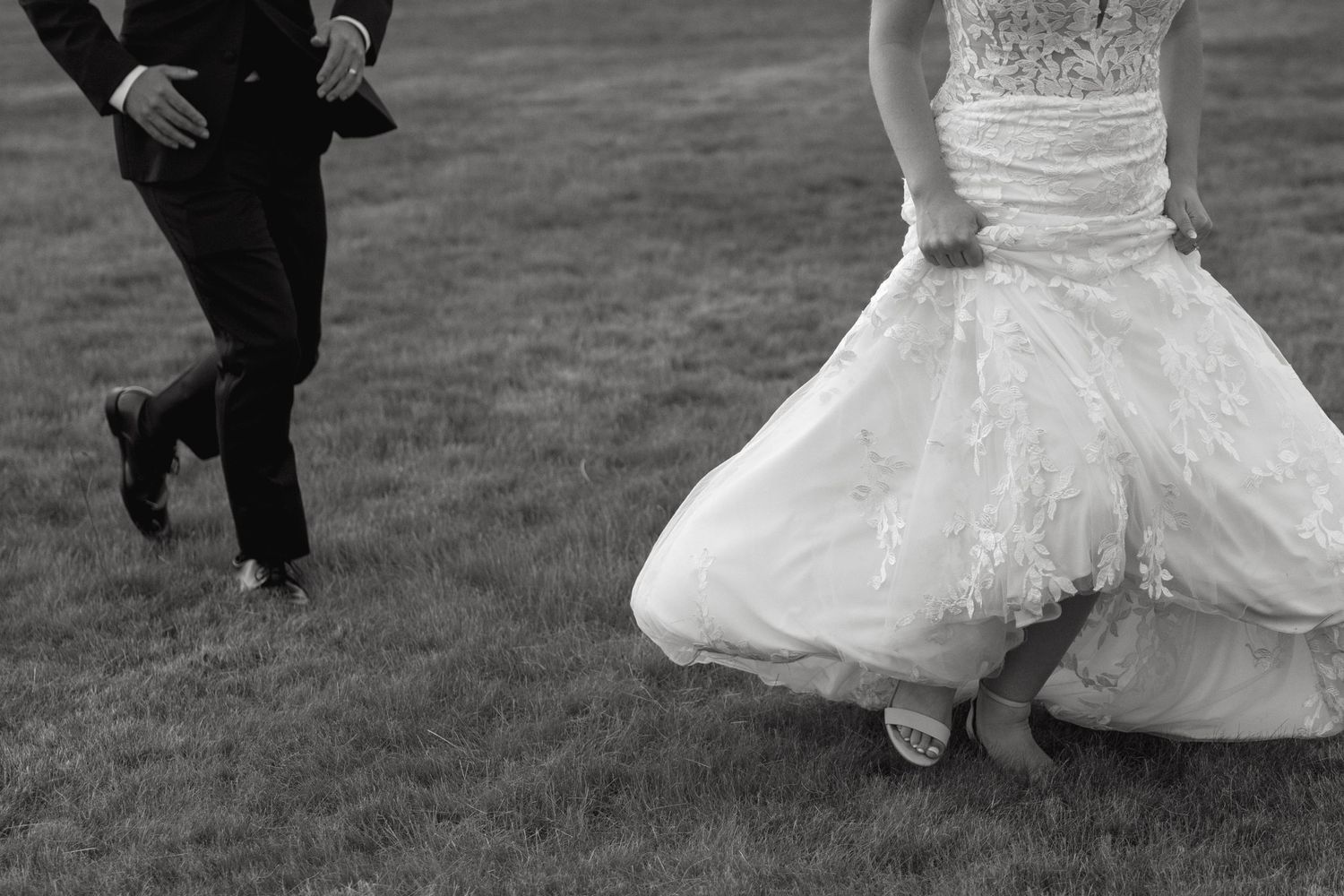 Bride in white gown twirls and dances outdoors on grassy field.