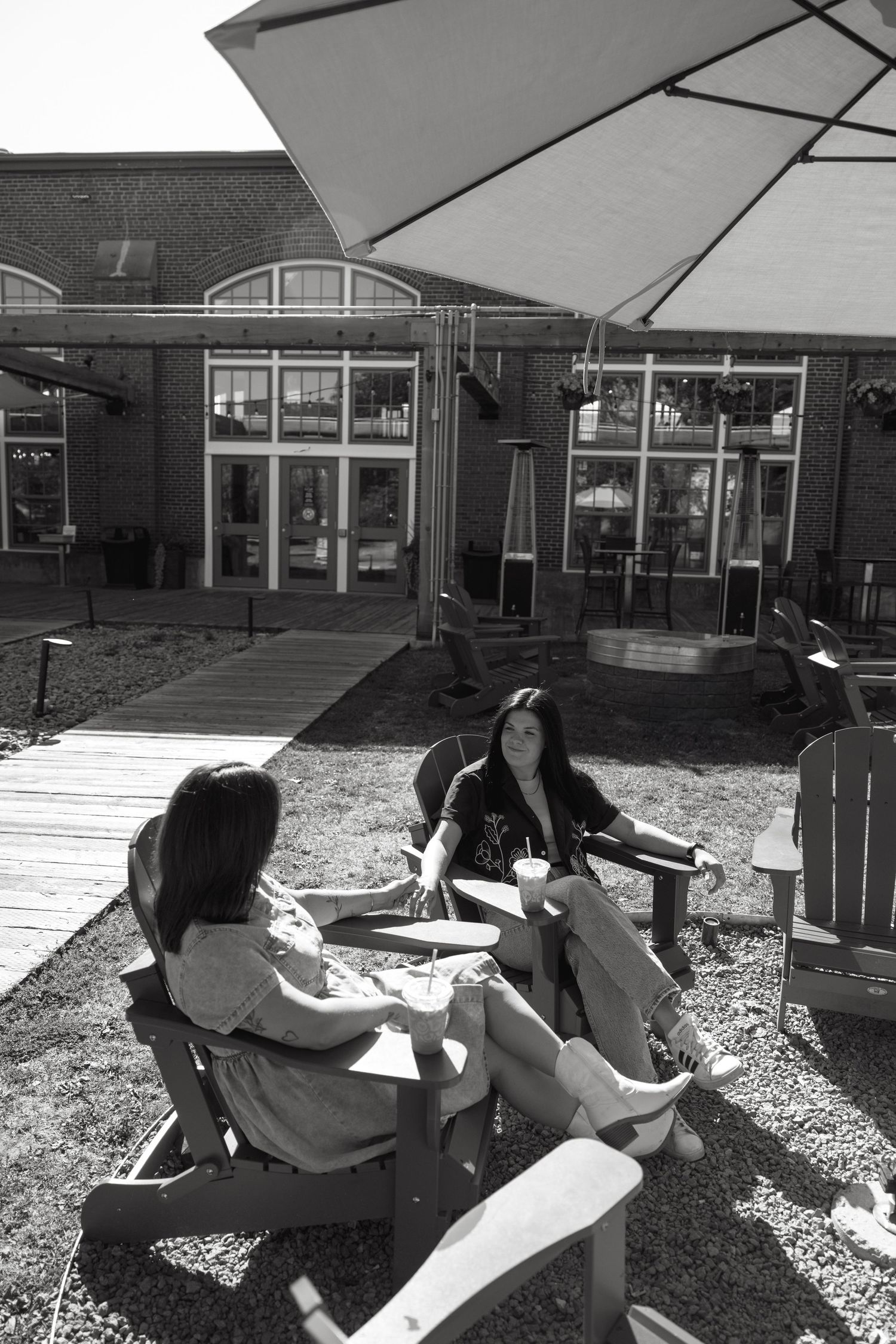 Black and white photo of people relaxing in outdoor chairs near a building.