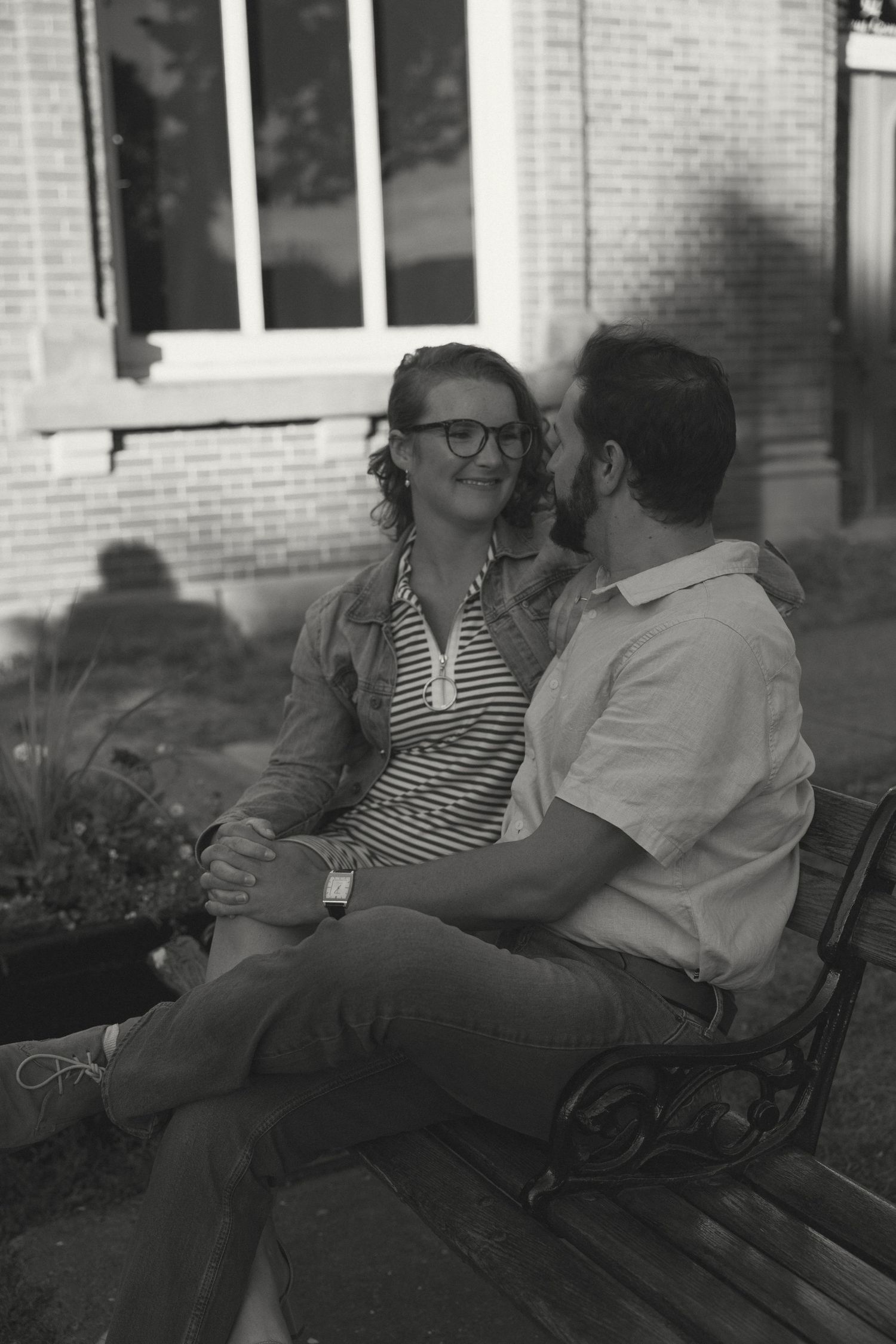 A couple sits close together on a bench in black and white photography.