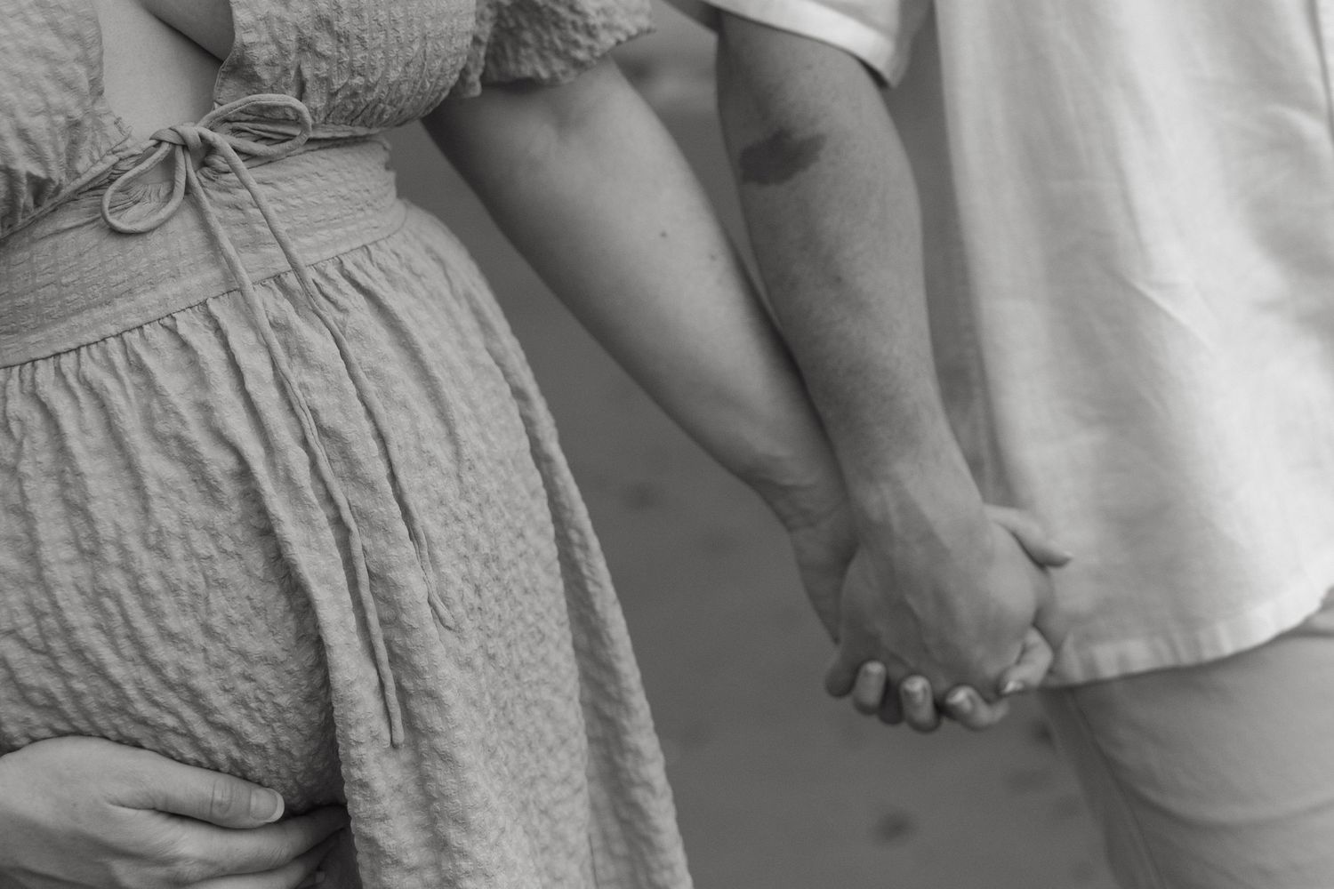 Close-up detail of casual beach attire and clasped hands during a seaside photoshoot.