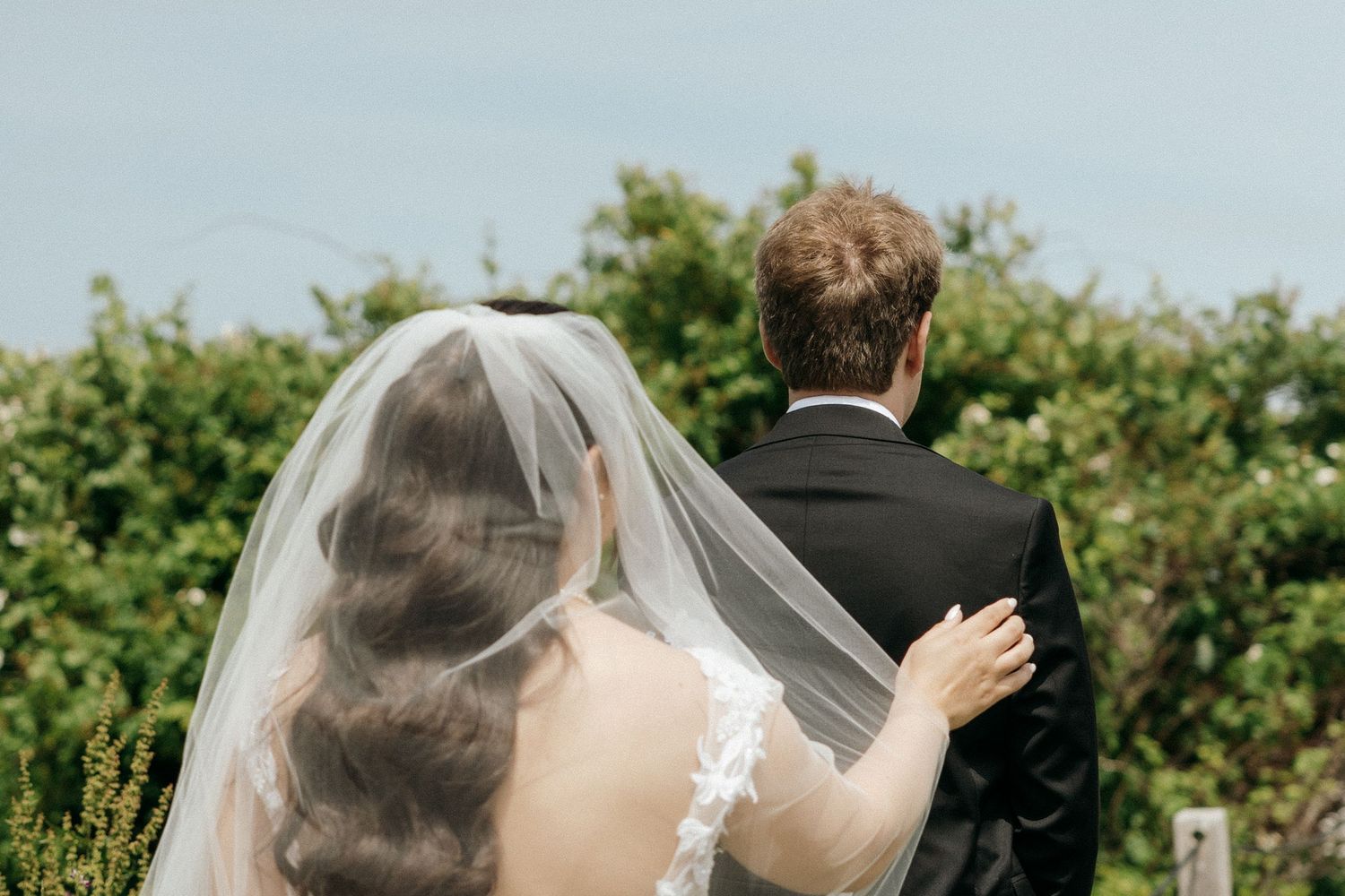 A flowing white wedding veil catches the breeze against a scenic coastal background.