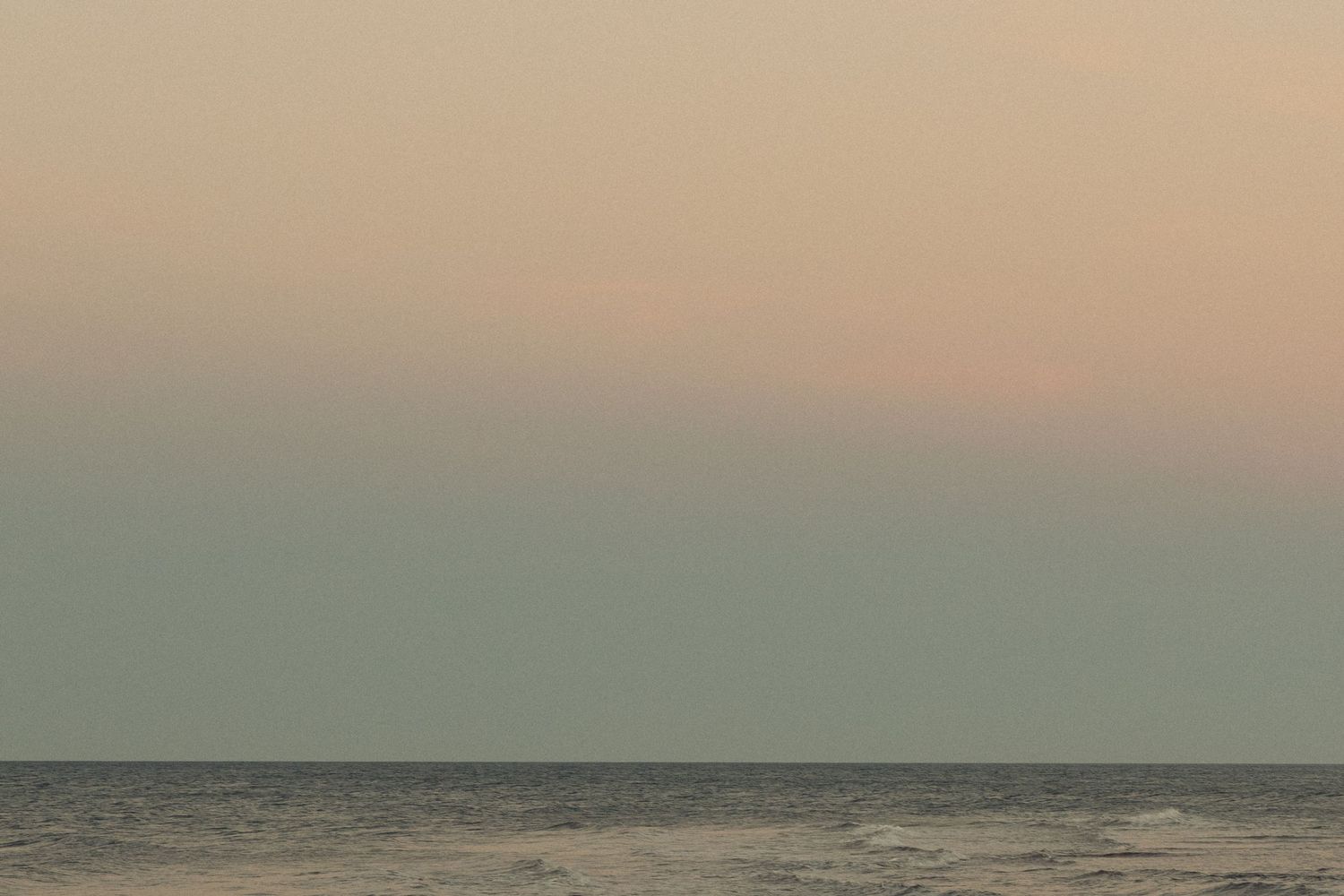 Serene ocean horizon at sunset with muted pink and teal colors in the sky.