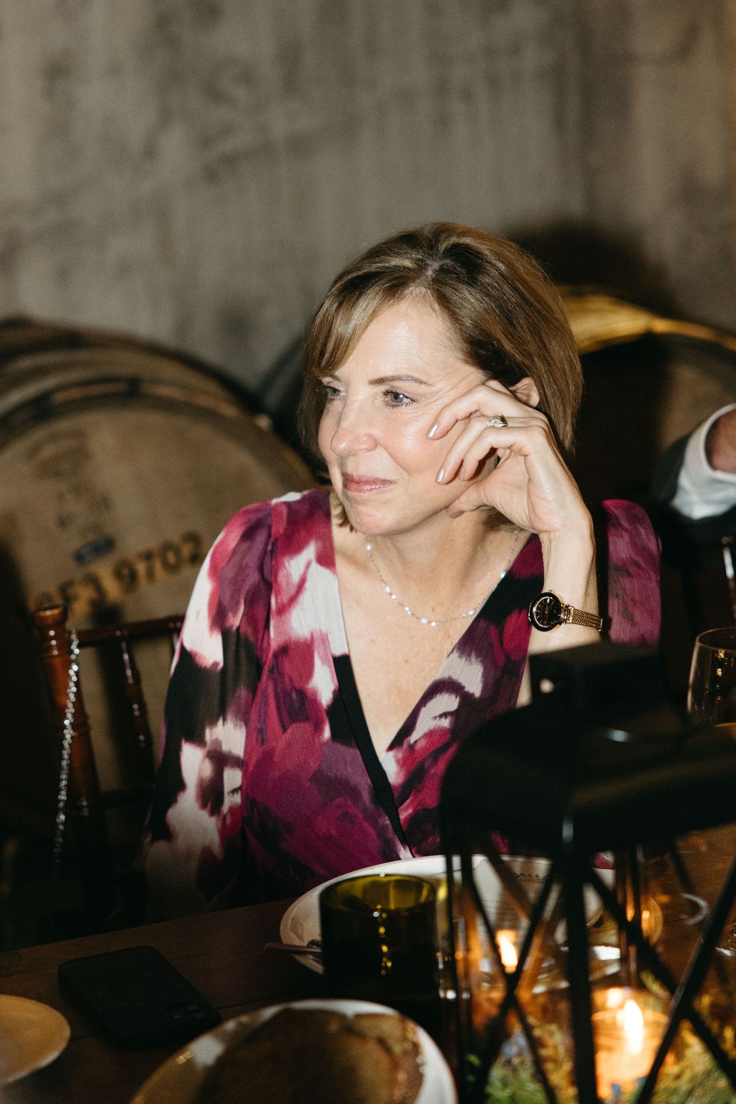 Guest in purple floral blouse enjoying conversation at candlelit dinner table.