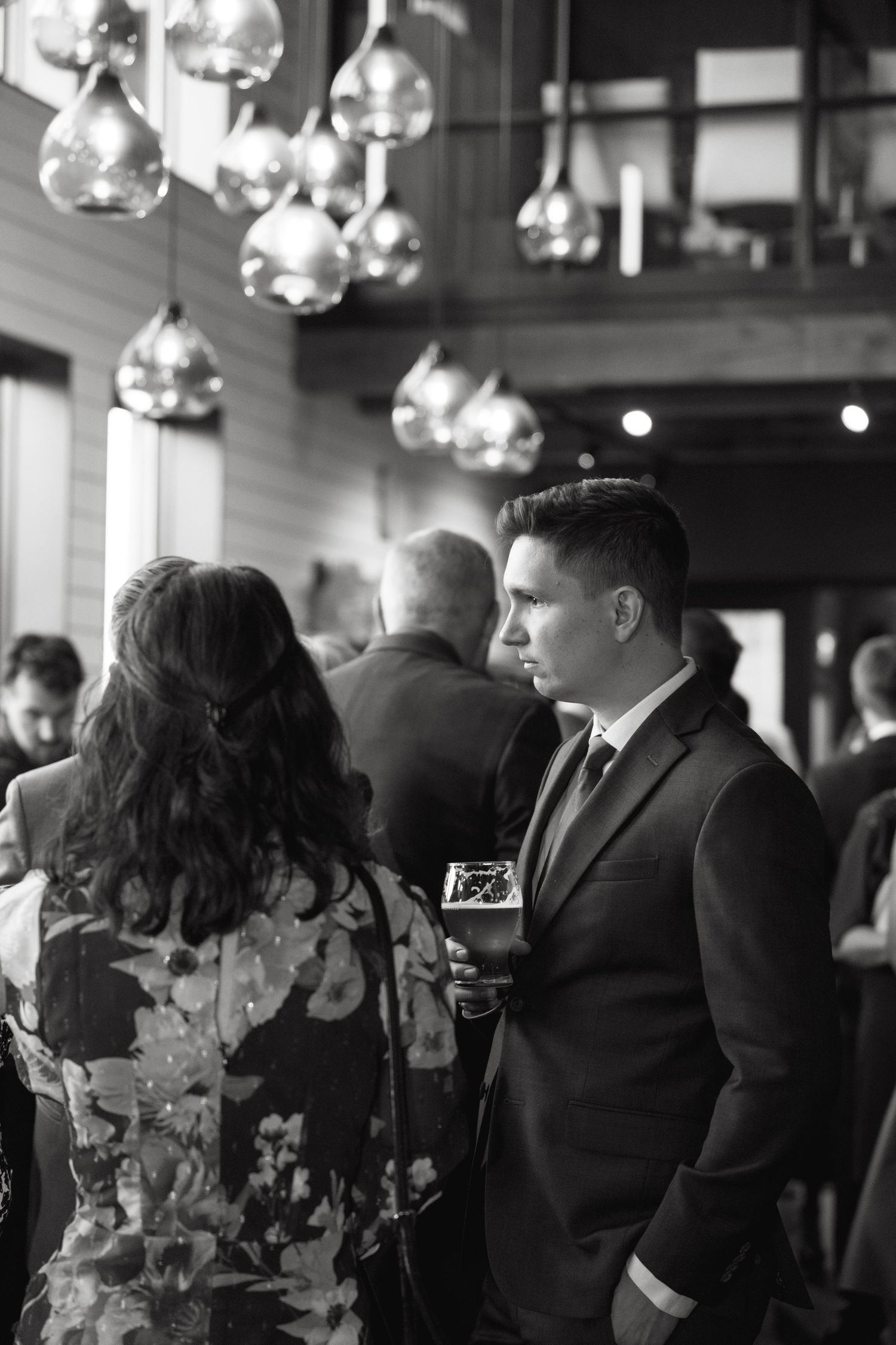 Wedding guests mingle at an elegant indoor reception with hanging crystal light fixtures.