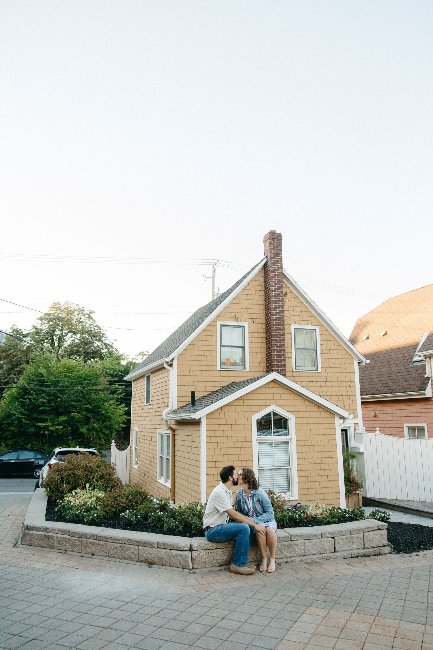 A couple sits together on stone steps outside a beige house.
