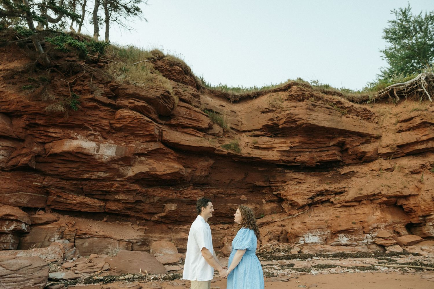 A couple holds hands during their beach photoshoot with red cliffs in the background.