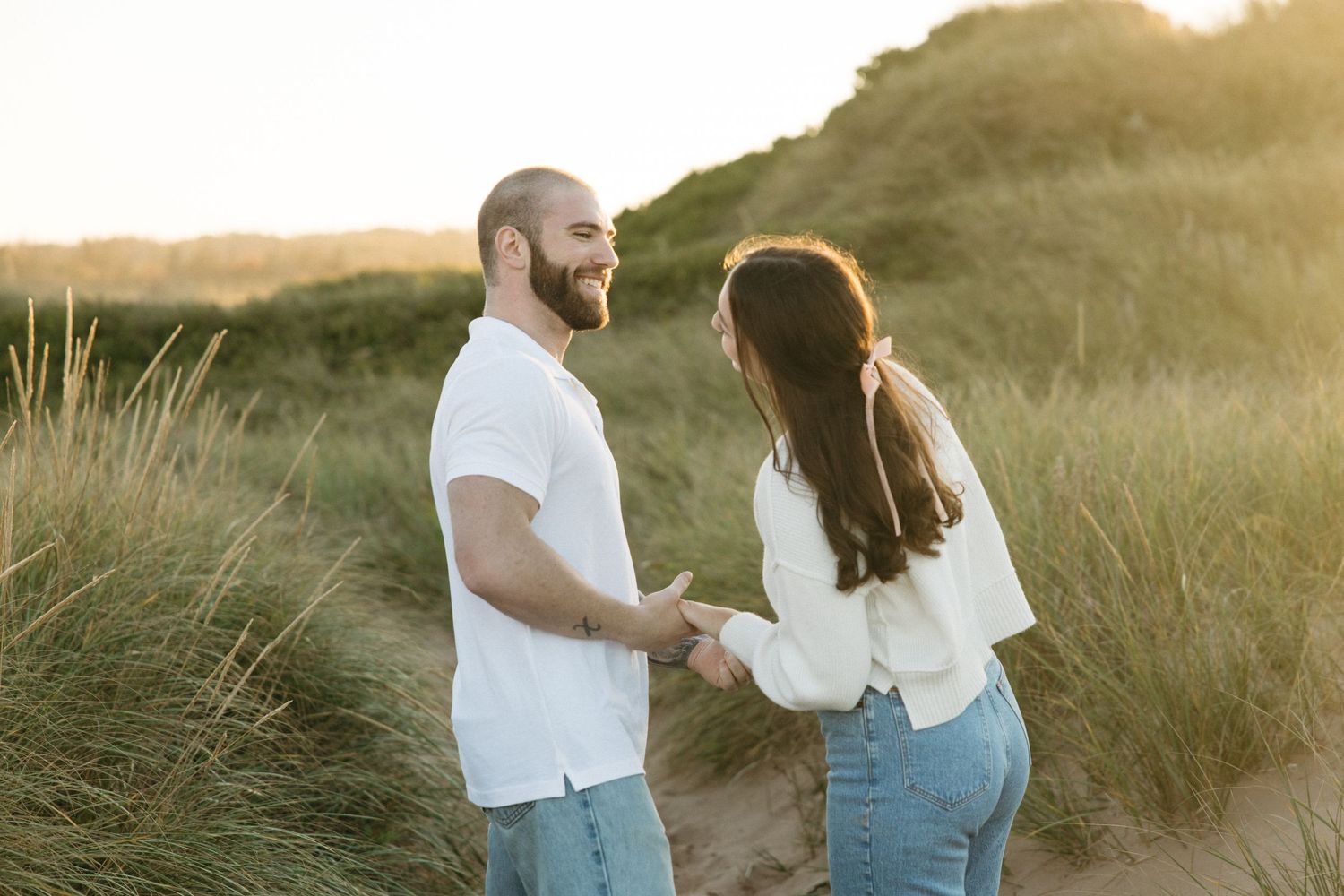 Couple enjoying intimate moment in beach grass during sunset photoshoot.