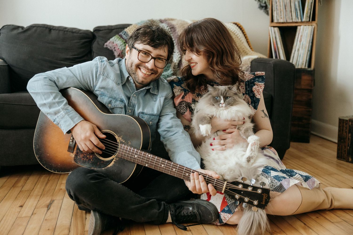 Cozy indoor scene with couple and cats relaxing with guitar and books.