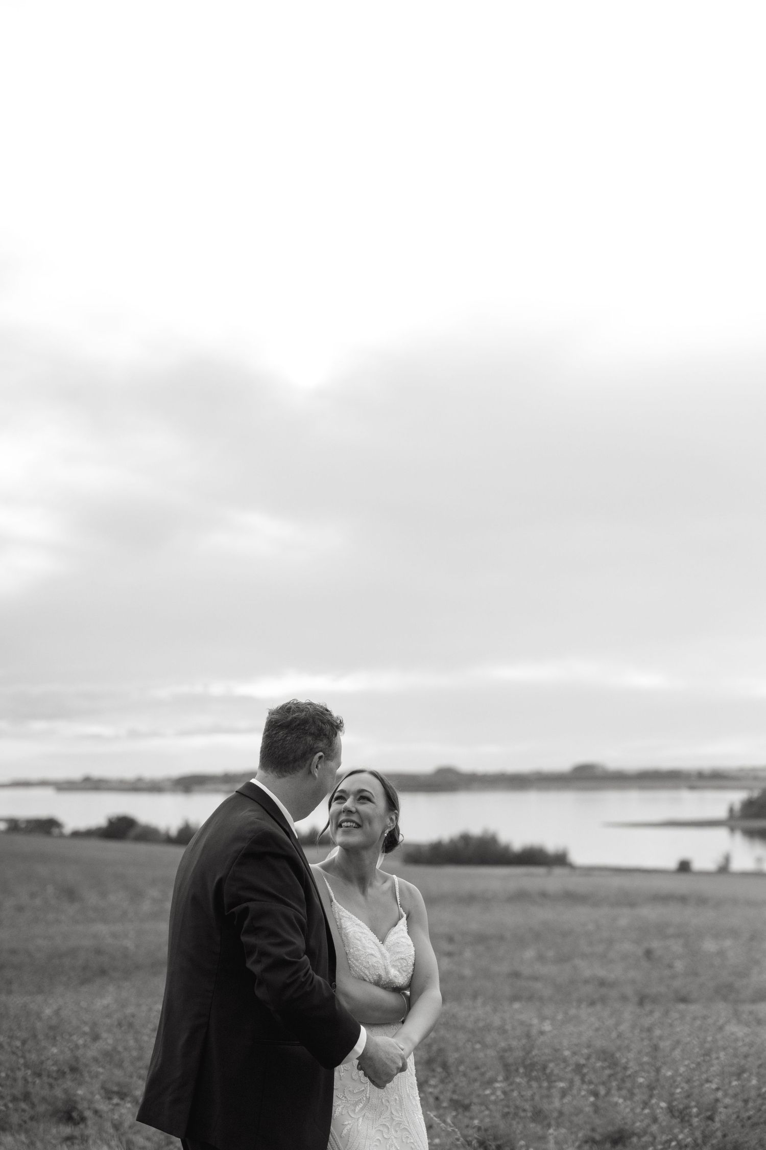 A black and white portrait of a couple sharing an intimate moment in a coastal field.