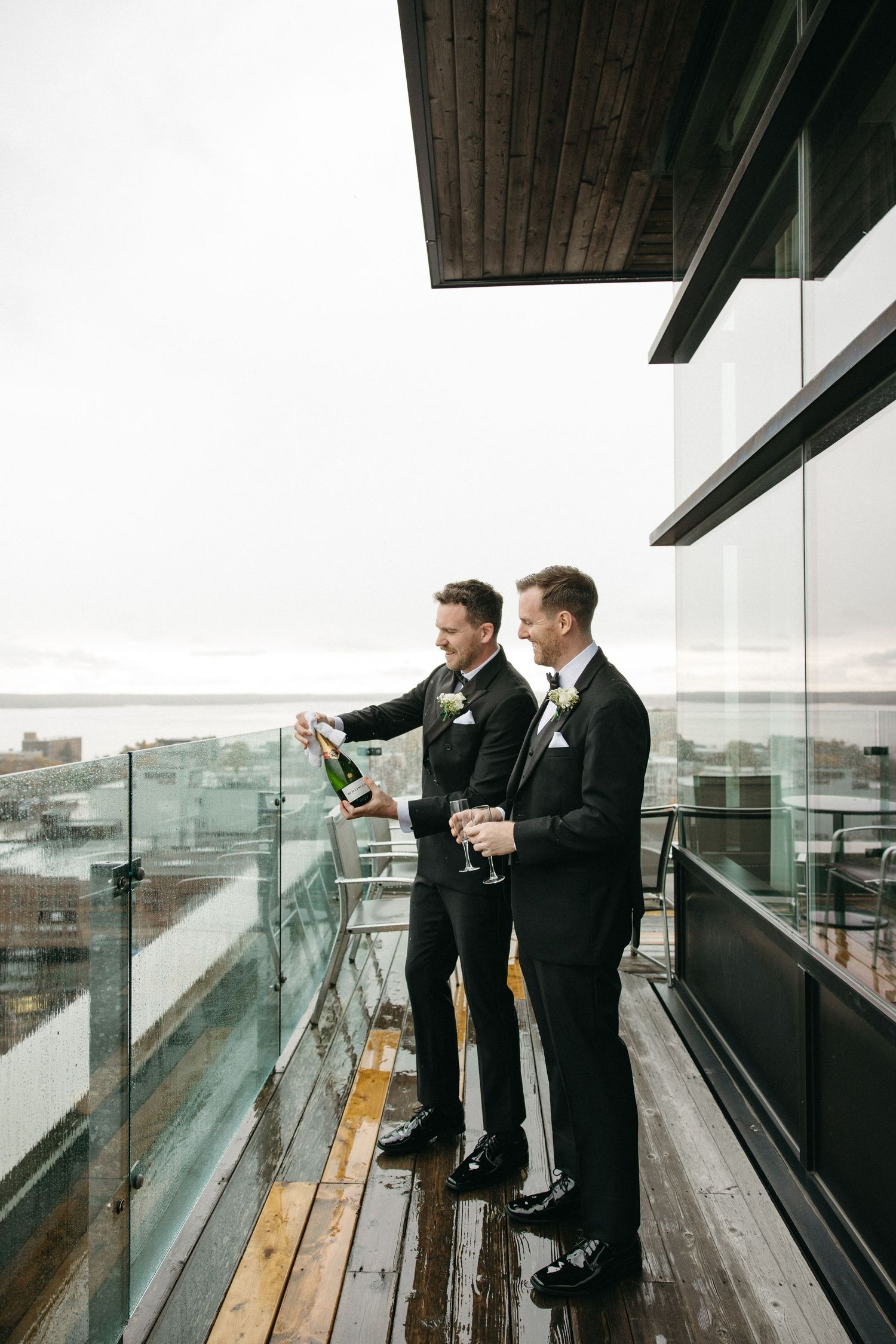 Two people in formal wear stand on a wooden deck overlooking a cityscape.