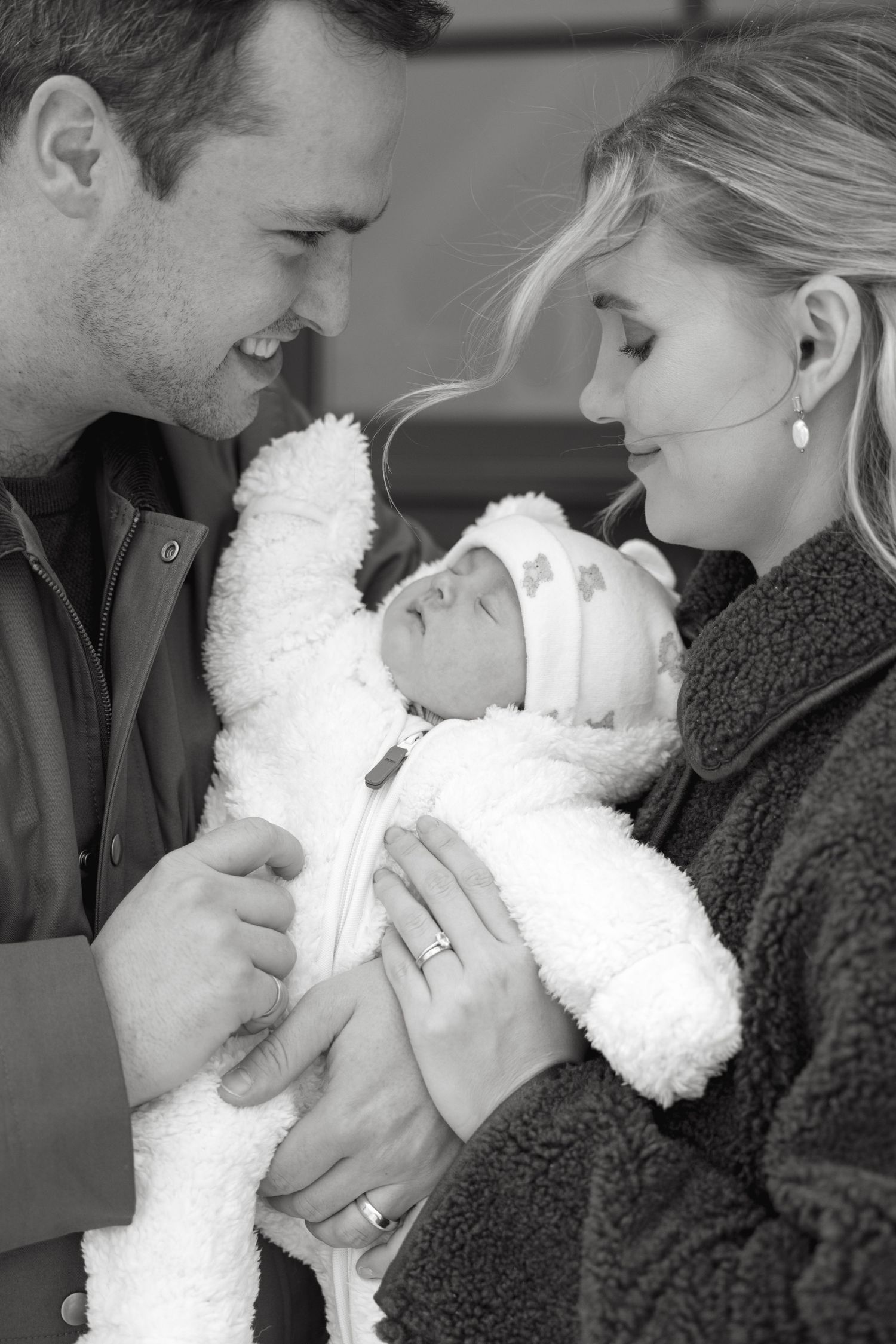 A tender family moment with a newborn baby wrapped in white, captured in black and white photography.