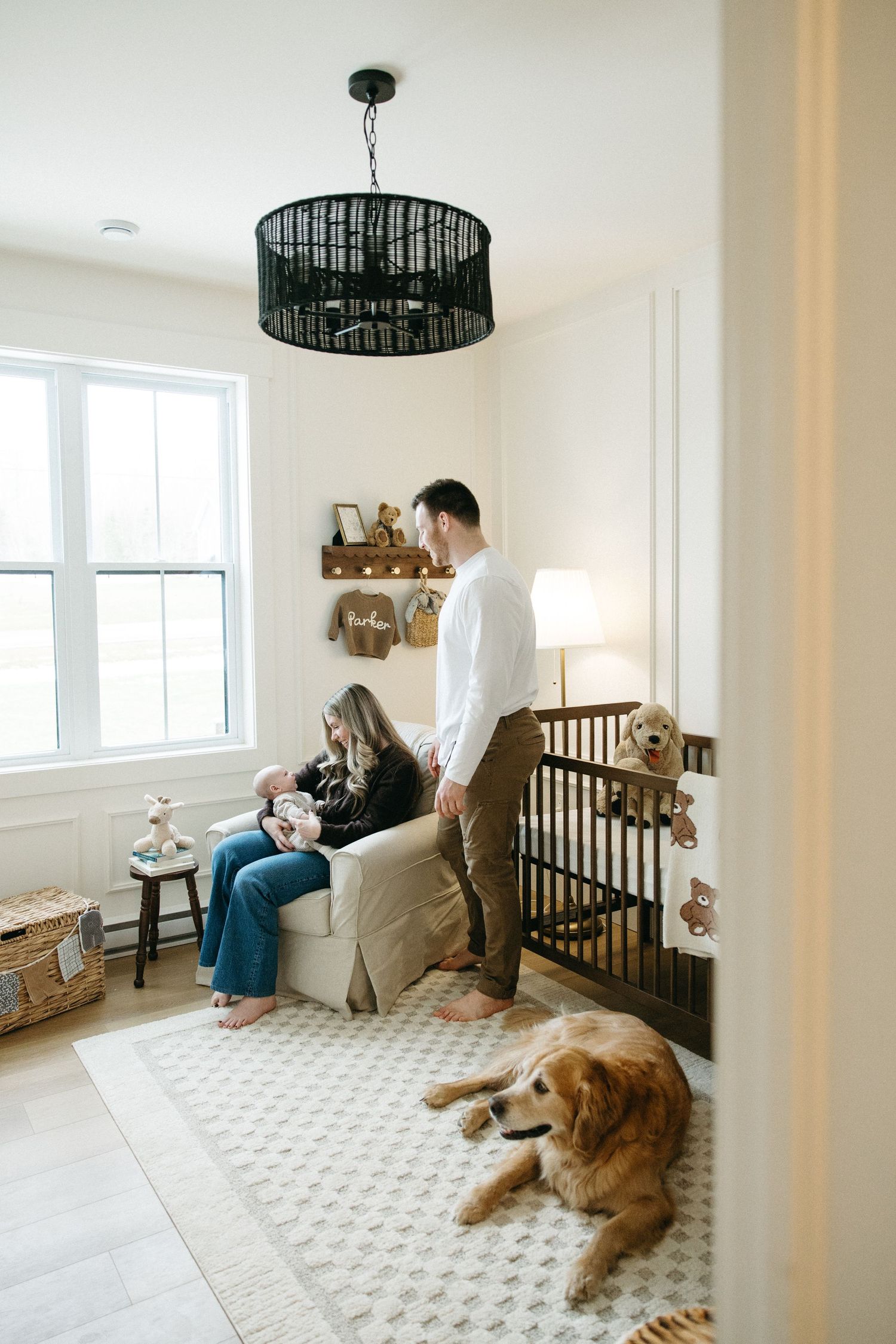 A cozy nursery room with a black drum pendant light, patterned rug, and golden retriever resting on the floor.