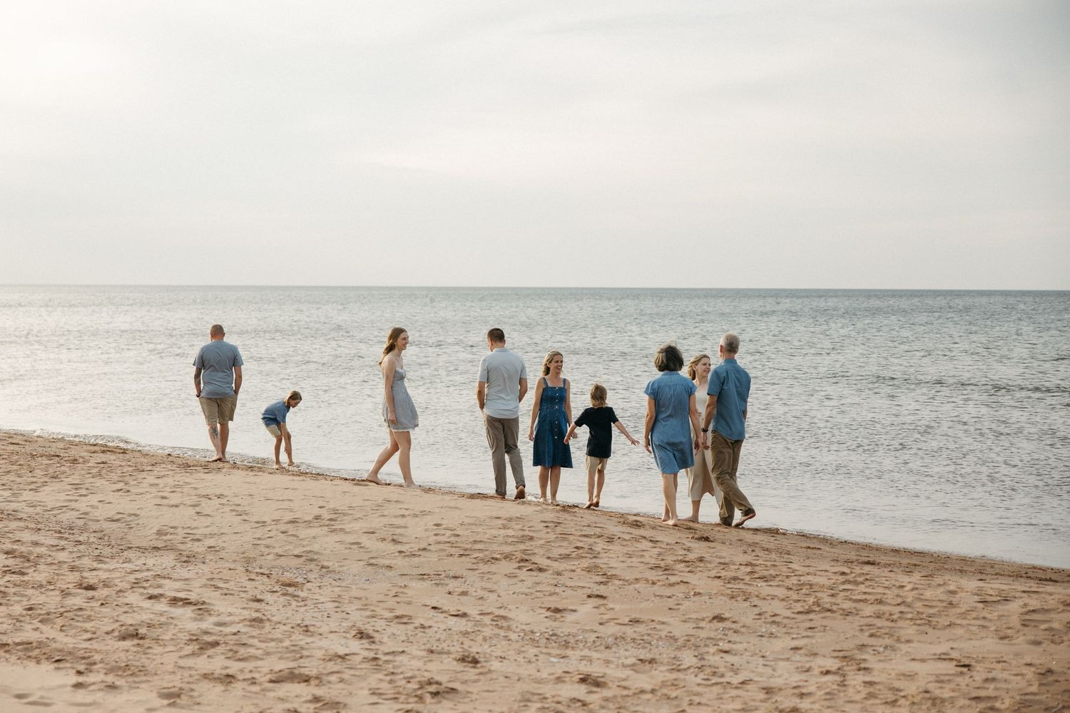 A large family in blue outfits walks along the shoreline at sunset on a sandy beach.
