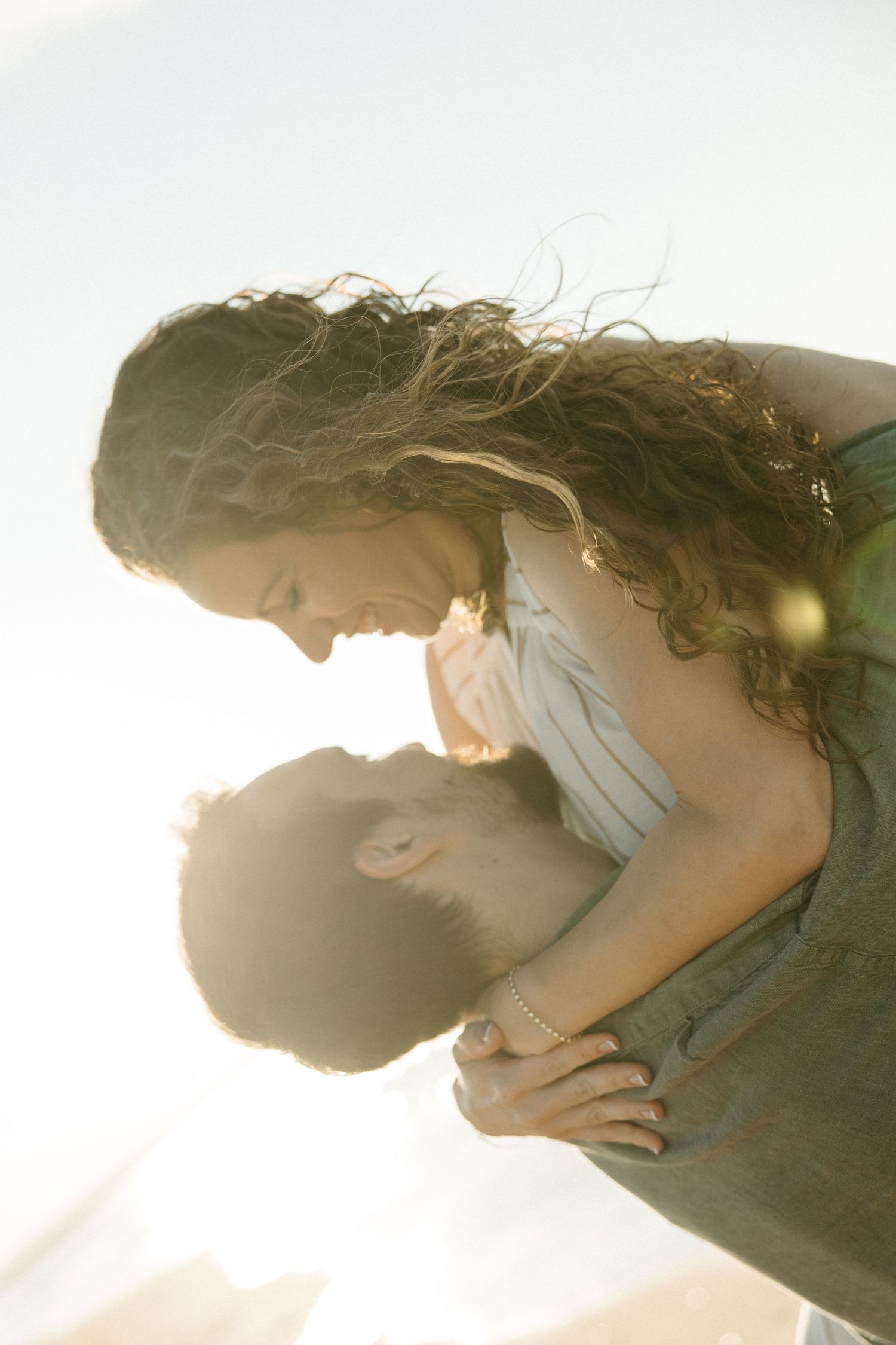 Romantic couple embracing in golden sunlight, man lifting woman as they lean in to kiss.