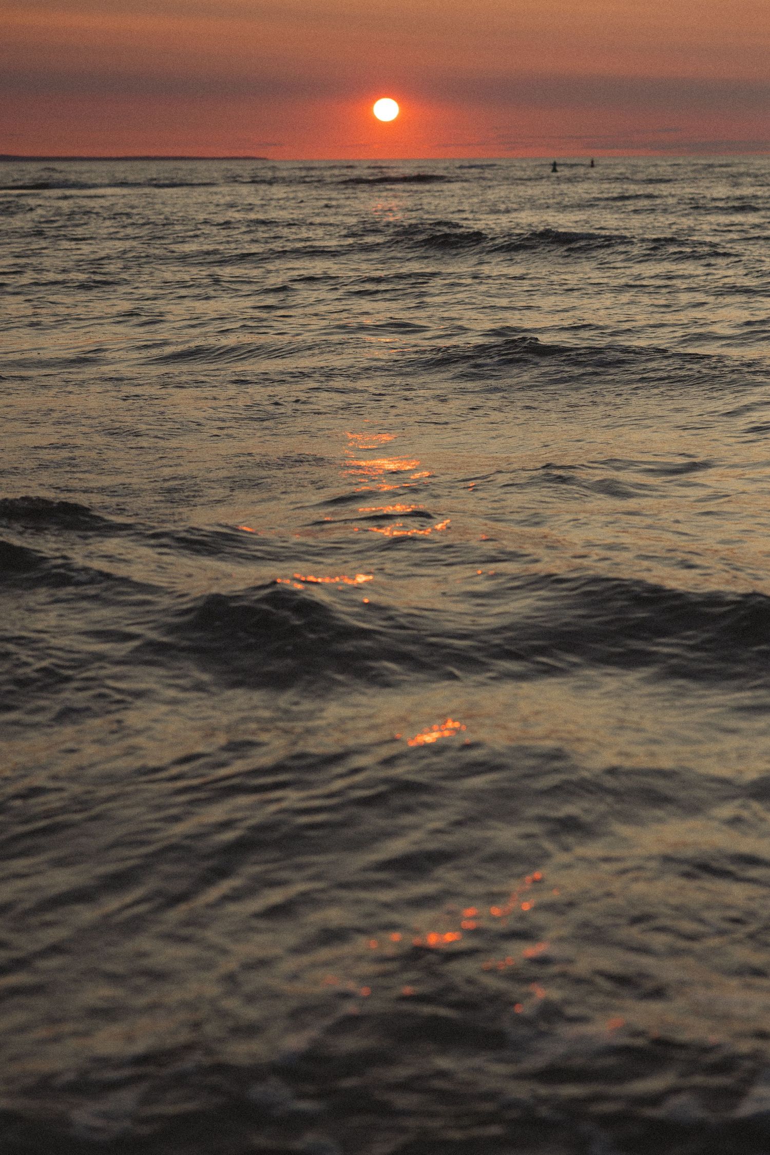 A stunning ocean sunset with a bright red sun on the horizon reflecting golden light across gentle waves.