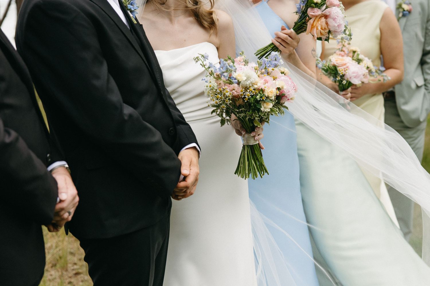 Wedding party holding pink and blue bouquets in white and black formal attire.